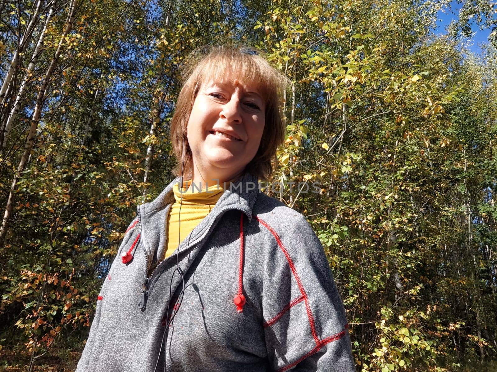 Blonde woman takes a cheerful selfie during her nature trip, surrounded by vibrant autumn foliage and trees.