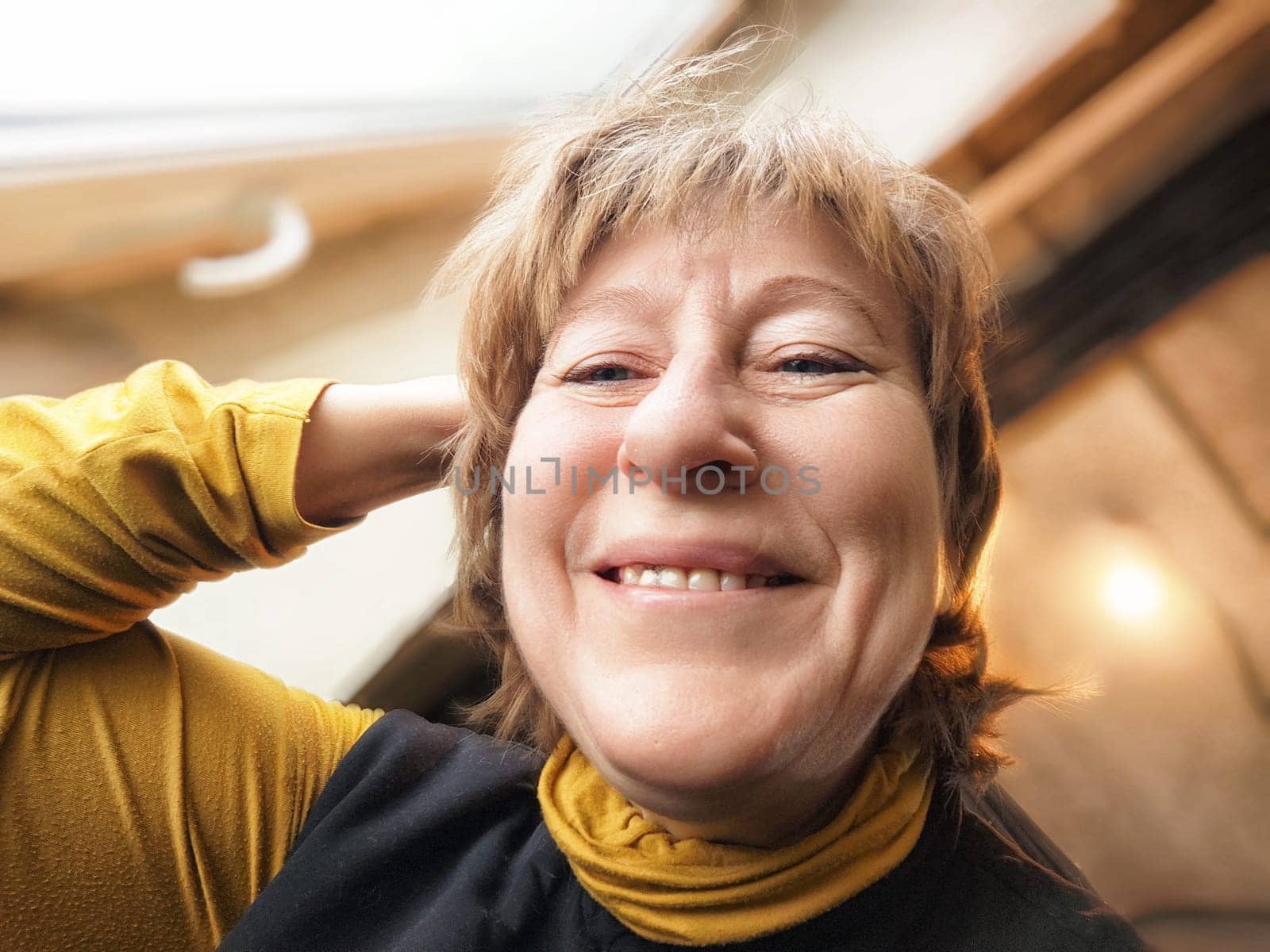 A blonde middle-aged woman takes a cheerful selfie, capturing her joyful moment during her latest travel experience.