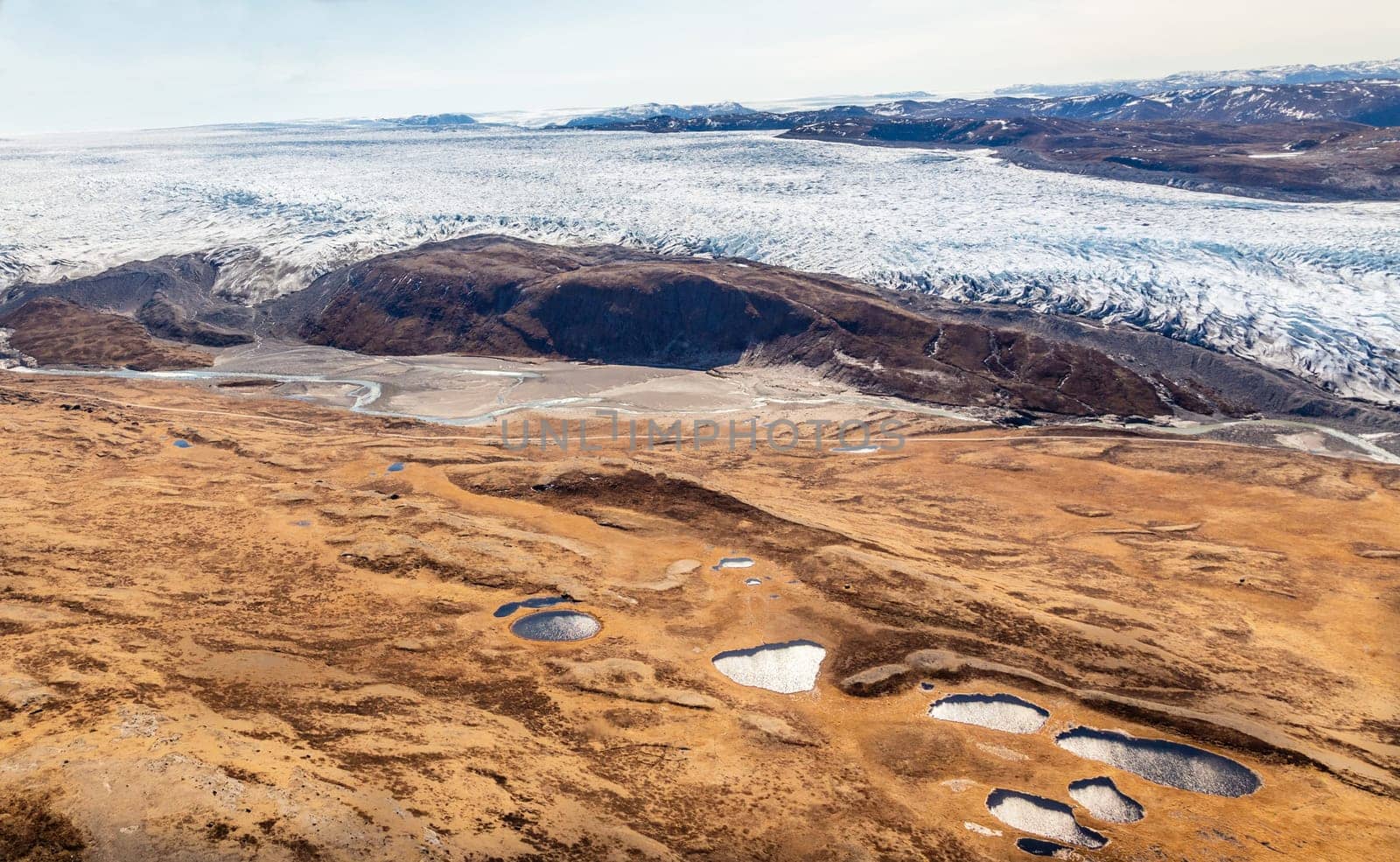 Greenlandic ice sheet melting glacier into river with tundra aerial view, near Kangerlussuaq, Greenland