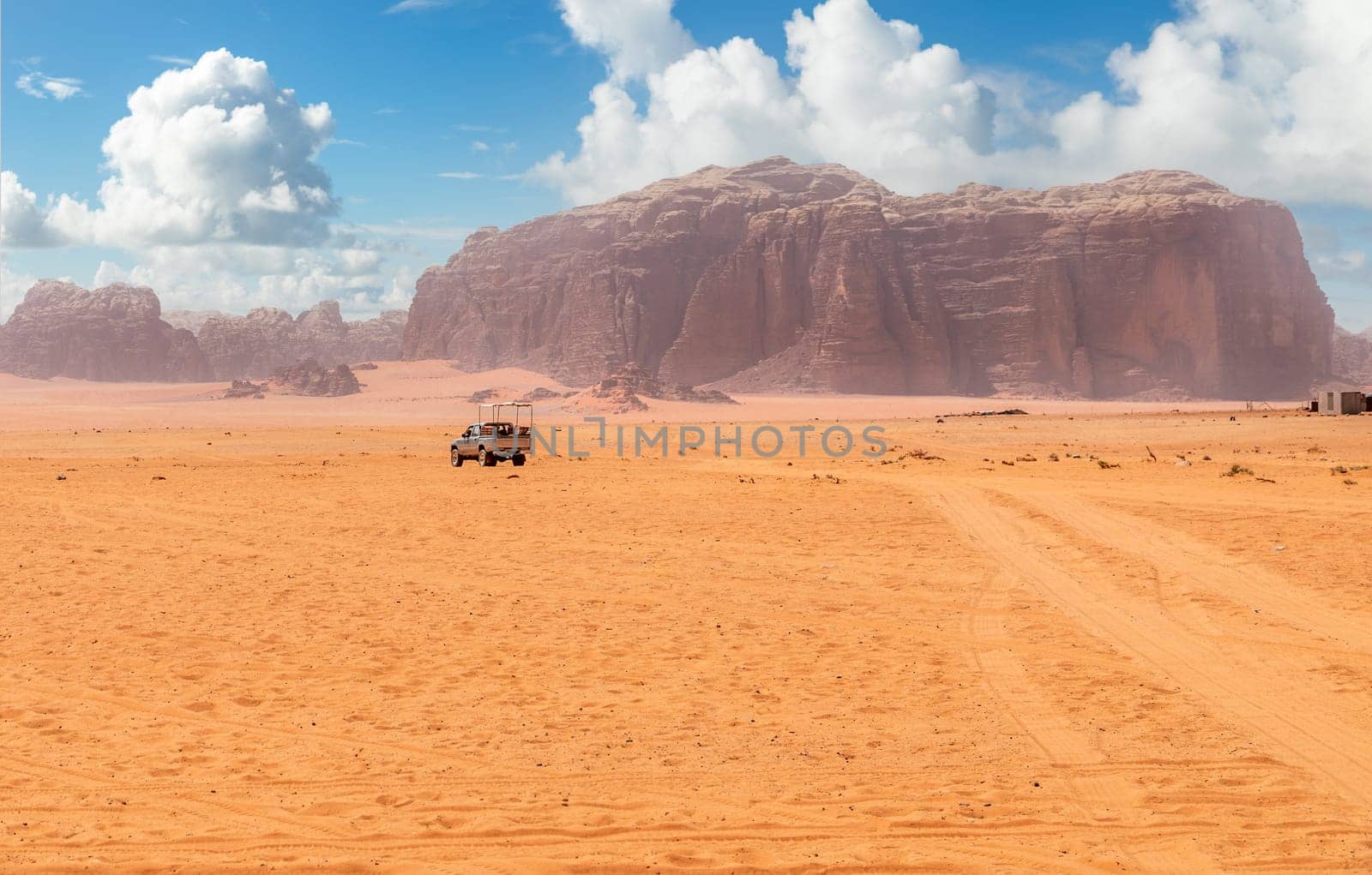 Orange sands and cliffs of Wadi Rum desert with tourist car in the background, Jordan
