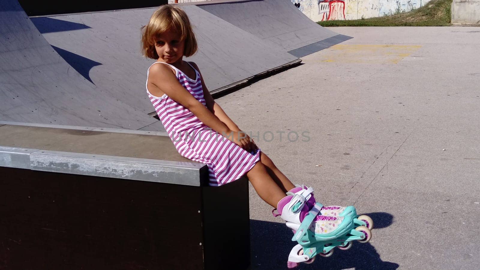 Sremska Mitrovica, Serbia, September 12, 2020. The girl is rollerblading on the asphalt. A 7-year-old child in a striped white and pink dress rides on roller skates on the playground