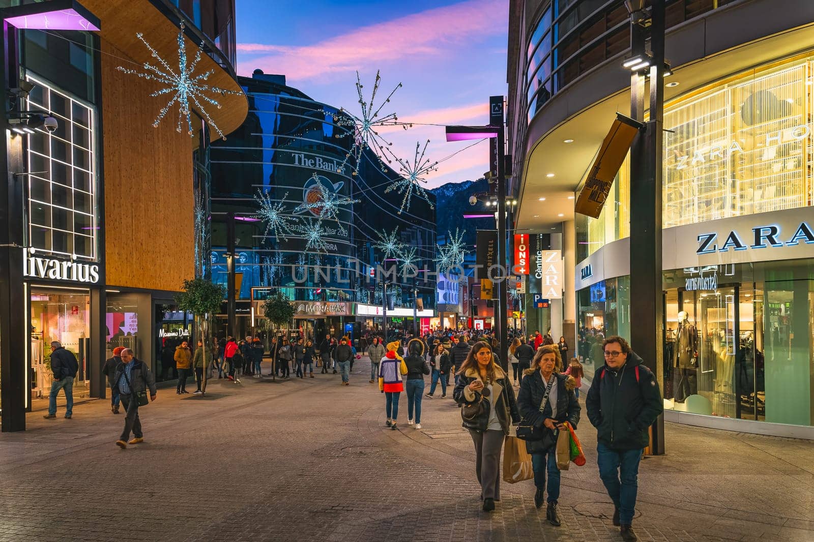 Andorra la Vella, Jan 2020 Crowd of people duty free shopping on street with modern shops and mall at night, illuminated by street lights, Pyrenees