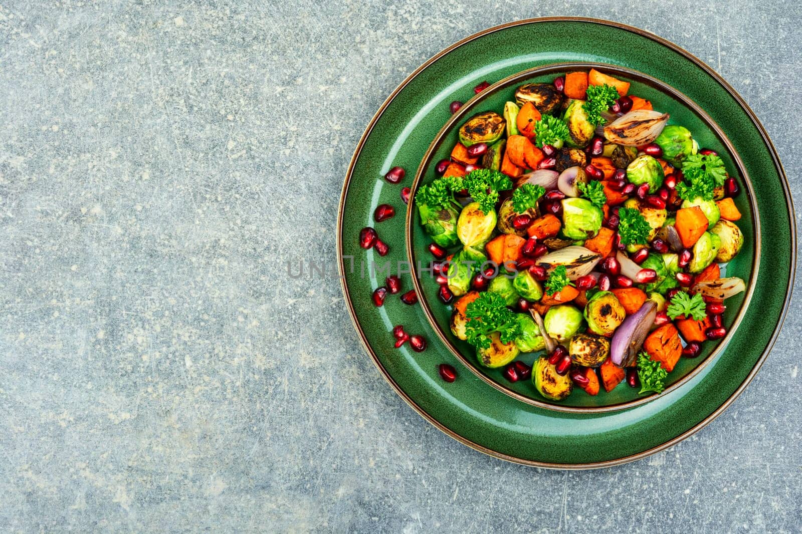 Salad with grilled brussels sprouts, grilled carrots, decorated with greens and pomegranate. Copy space, vegan menu