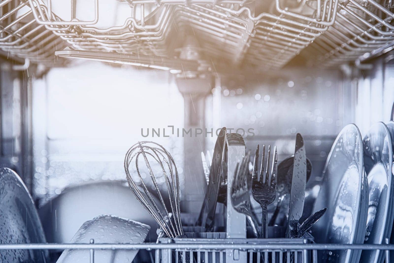 Front view of open automatic stainless steel built-in fully integrated top control dishwasher range machine with clean utensils, cutlery, glasses, dishes, plates inside in modern home kitchen