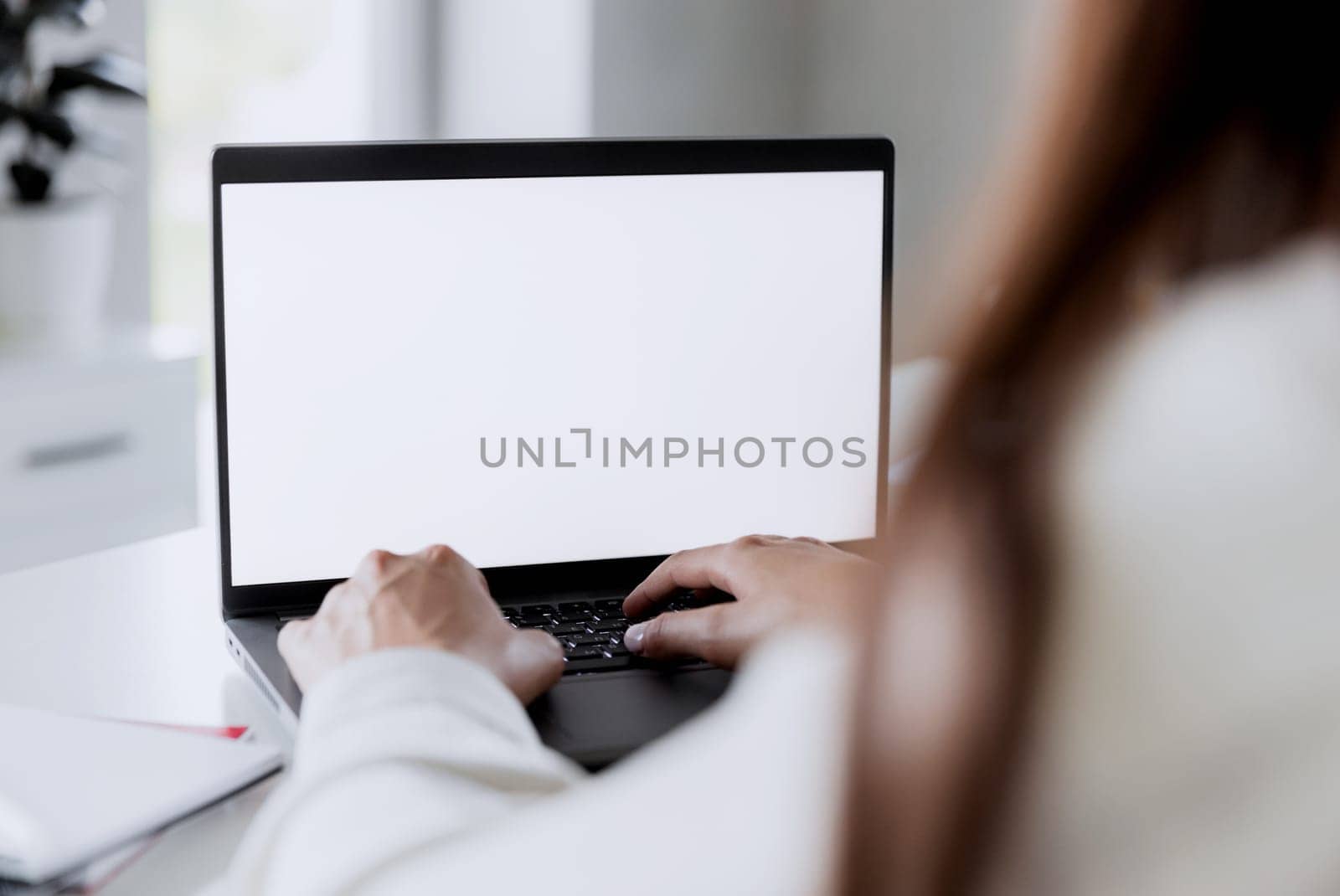Woman hands typing on the laptop with empty blank white screen mockup. Computer is laying on the white table. Blurred background. Person working from home concept. Copy space area for text