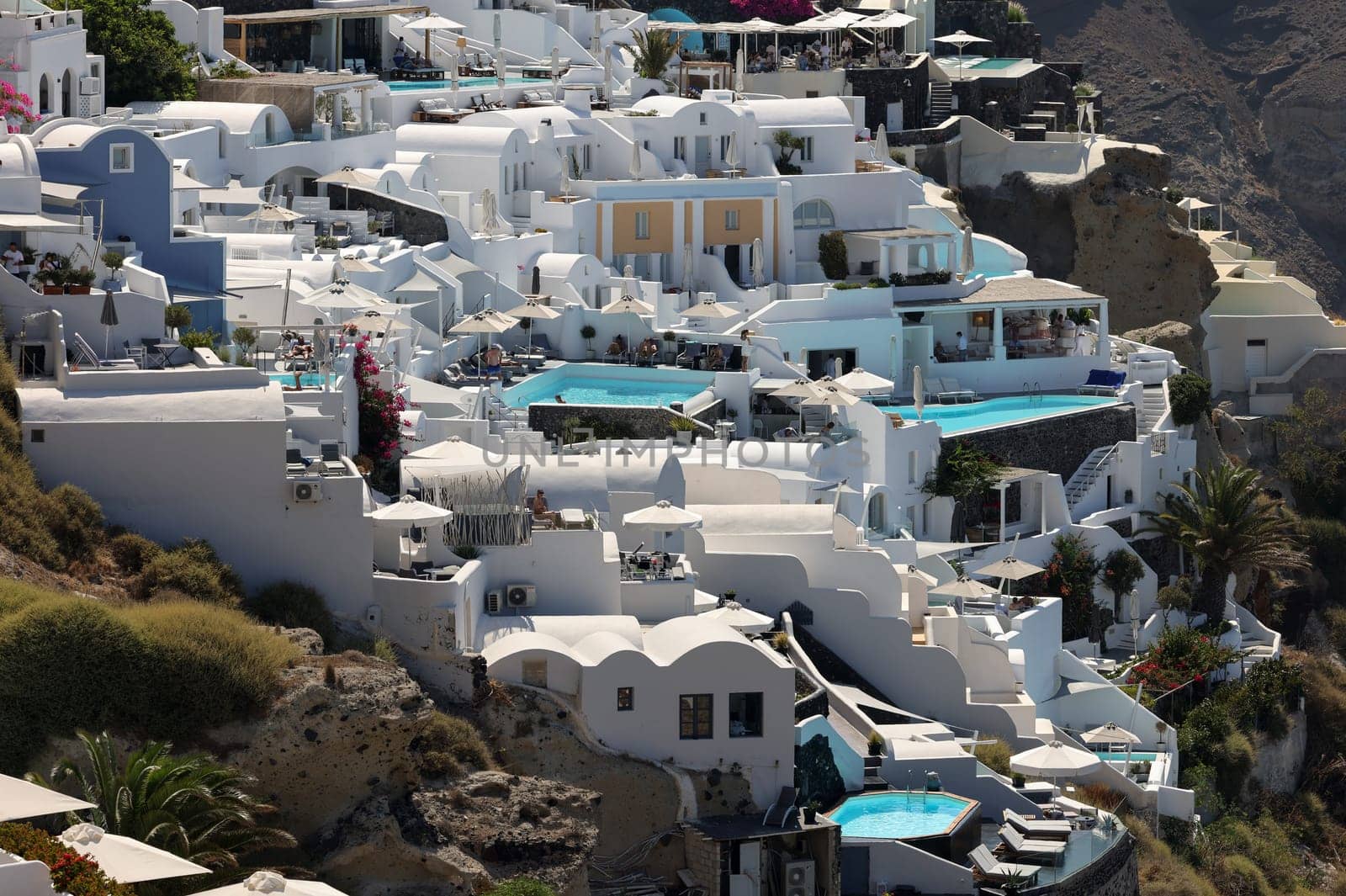 Oia, Santorini, Greece - July 3, 2021: Whitewashed houses with terraces and pools and a beautiful view in Oia on Santorini island, Greece