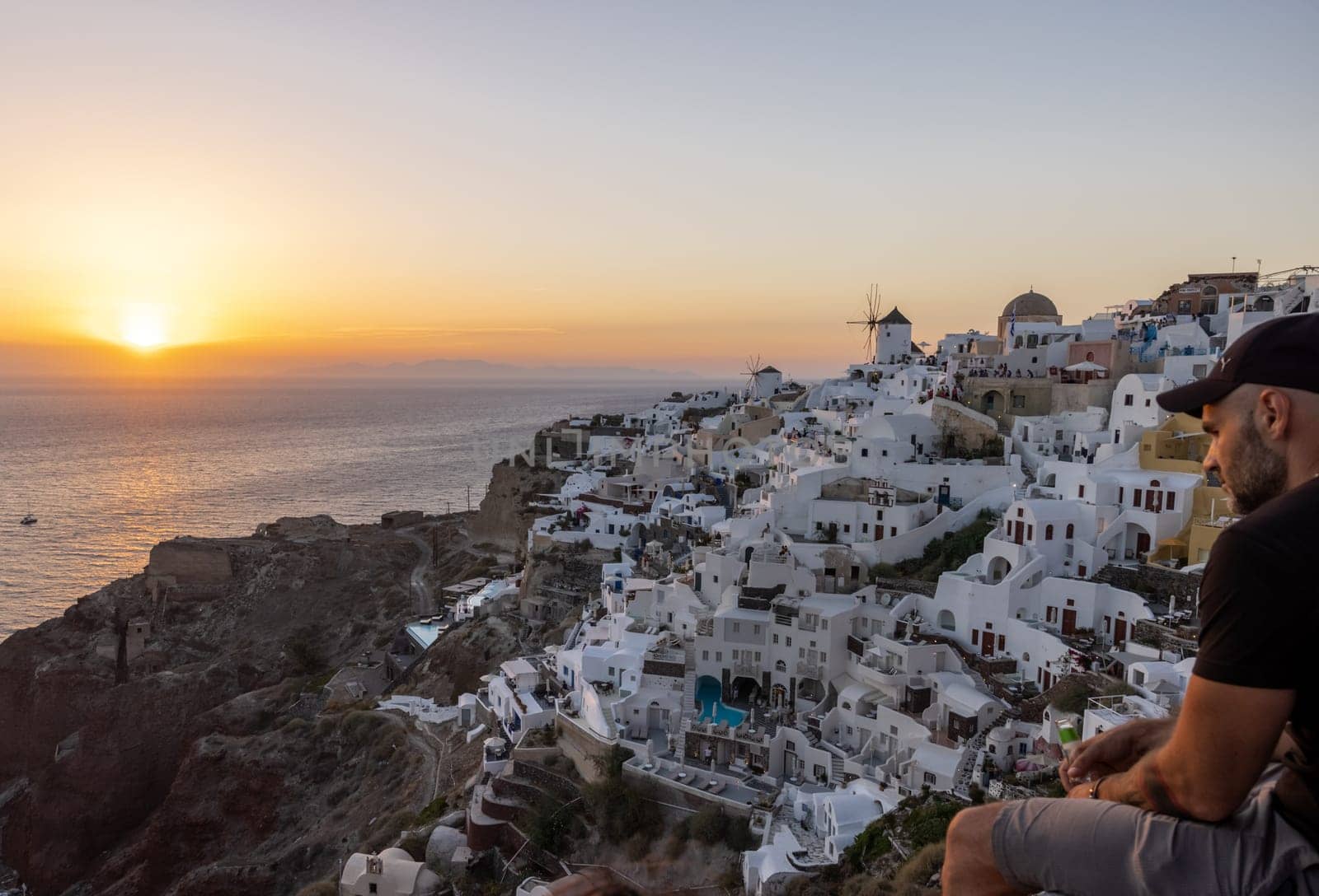 Oia, Santorini, Greece - June 28, 2021: Whitewashed houses and windmills in Oia in warm rays of sunset on Santorini island. Greece