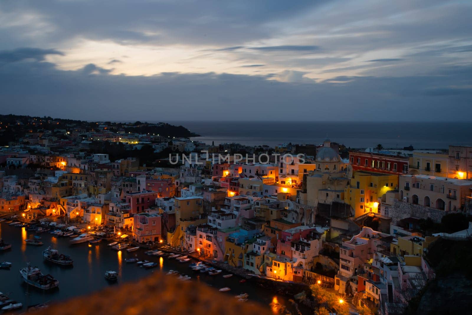 View of the Port of Corricella with lots of colorful houses after sunset in Procida Island, Italy.