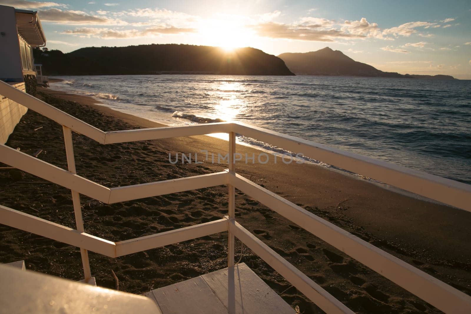 Wooden steps down to beach with waves and sand and island in the sunset.