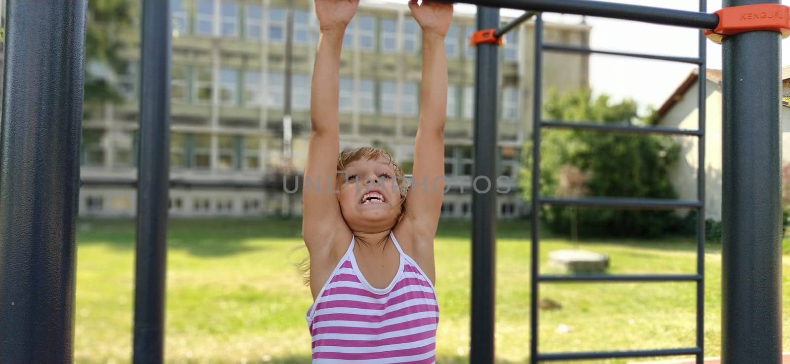 Sremska Mitrovica, Serbia, September 15, 2020 A child in a striped dress hangs on a metal bar and tries to pull up on his arms. Sports or playground. Outdoor exercise
