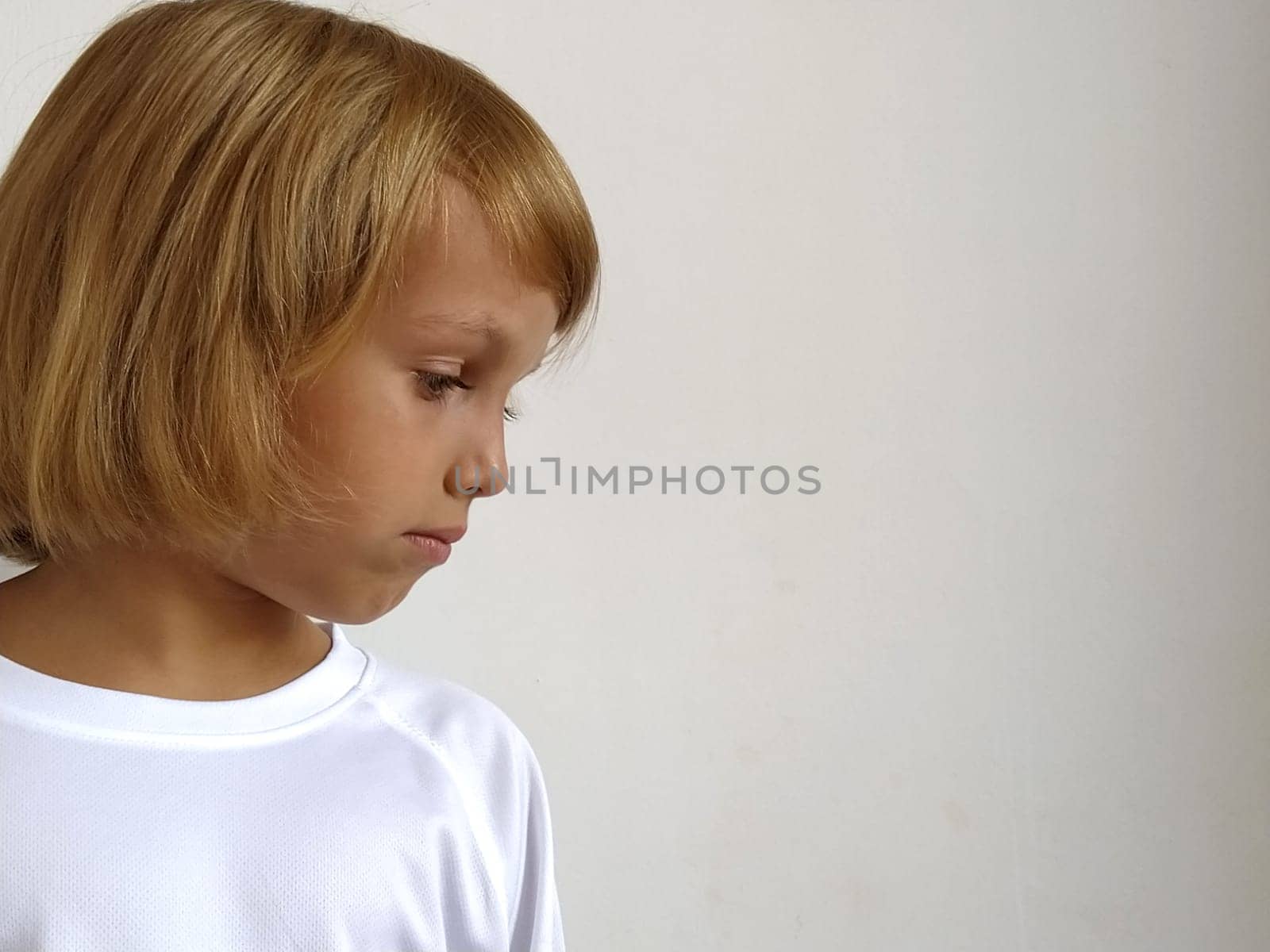 Girl on a white background. The child looks down and to the side. Copy space. White T-shirt. Caucasian blond hair, dark tanned skin. Head side. Bob hairstyle.