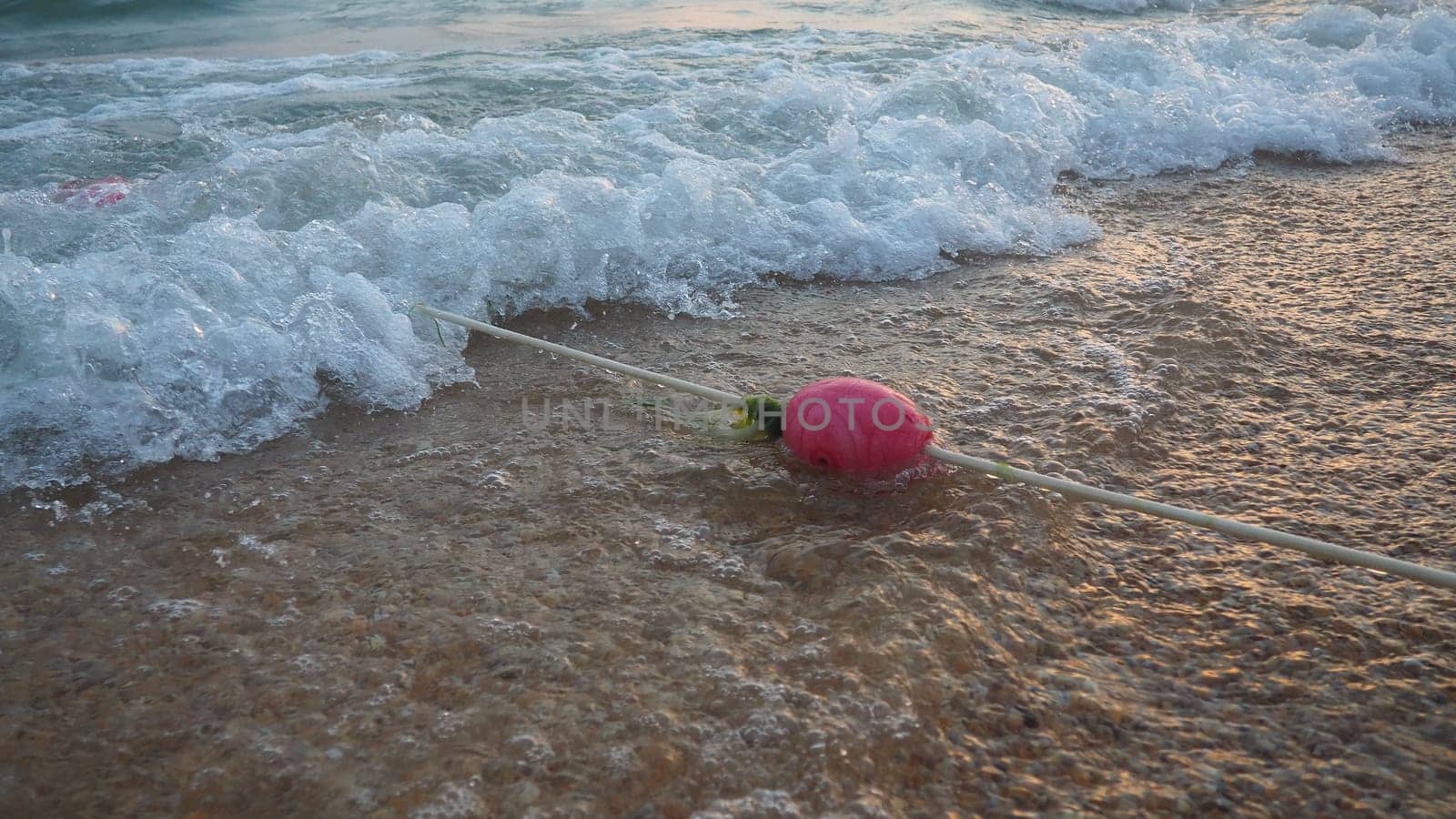 Buoys on a rope near sea water. The buoys are pink restraints to alert people to the depth of the water. Rescue of the drowning. Delimiting a place on a sandy beach between hotels. Wave with bubbles