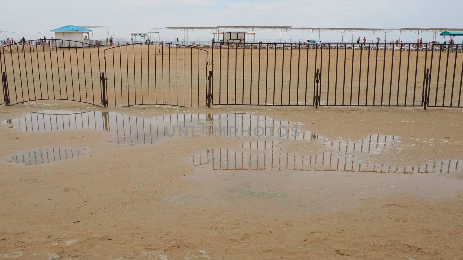 Vityazevo, Russia, August 10 2021 A puddle on a sandy quartz medicinal beach after heavy rain. Consequences of bad weather and typhoon. The edge of the beach holiday season. Tourists in the background