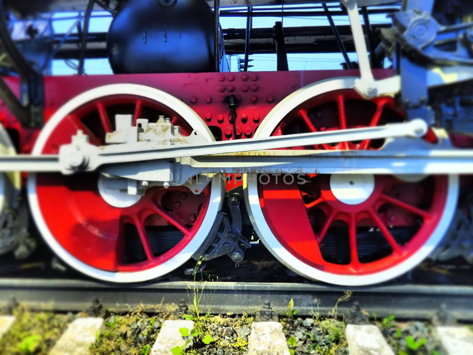 Retro vintage wheels of a locomotive or train close up. Red large heavy metal wheels with piston guiding mechanisms. Locomotive of the 19th - 20th centuries with a steam engine. Bright vivid photo.