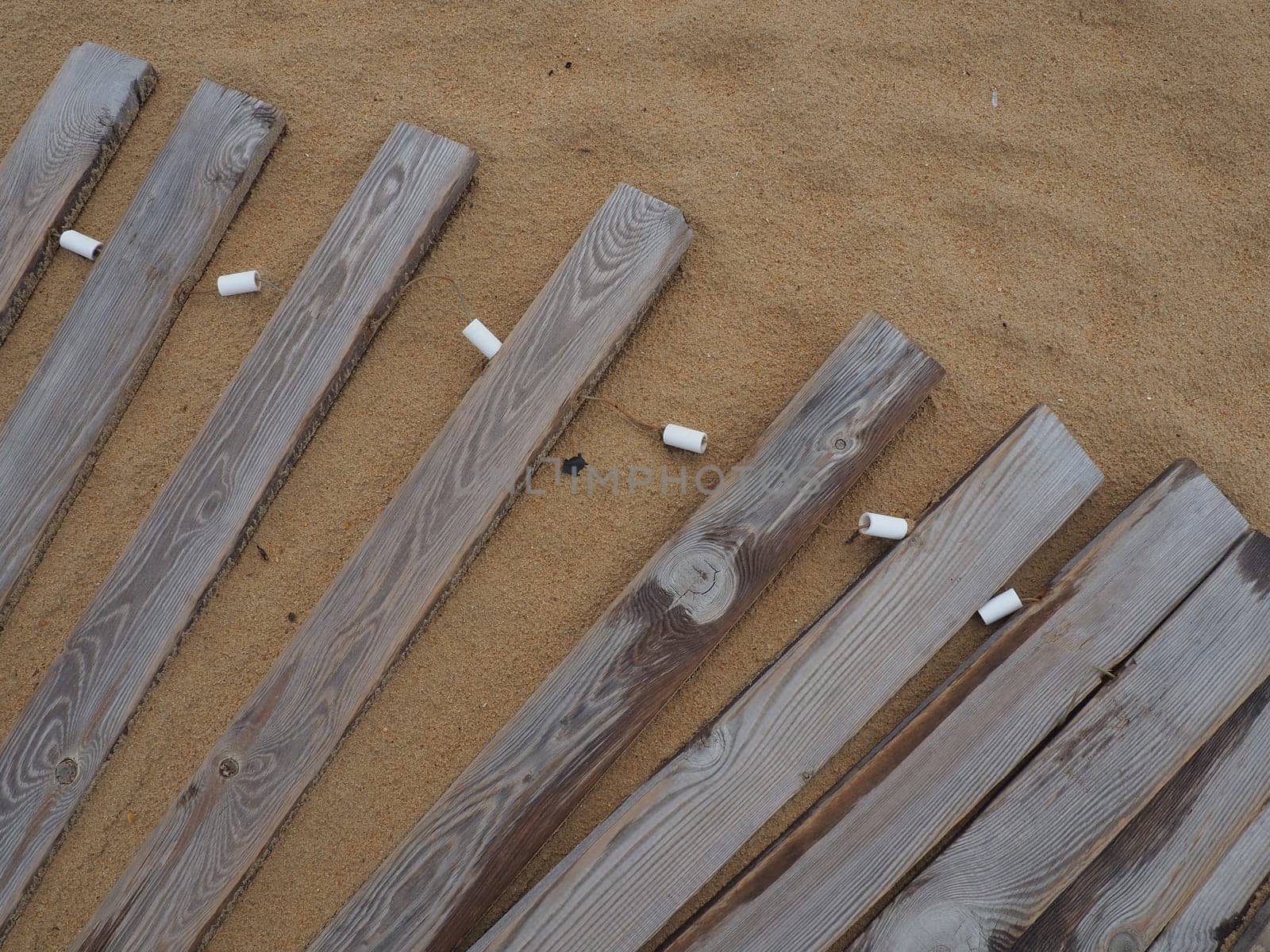 Wooden footbridge on a sandy beach. Uneven, damp wooden planks held together. The edge of the beach season at the hotel. No people, copy space. Equipped sandy beach after a storm or cyclone. Tourism.