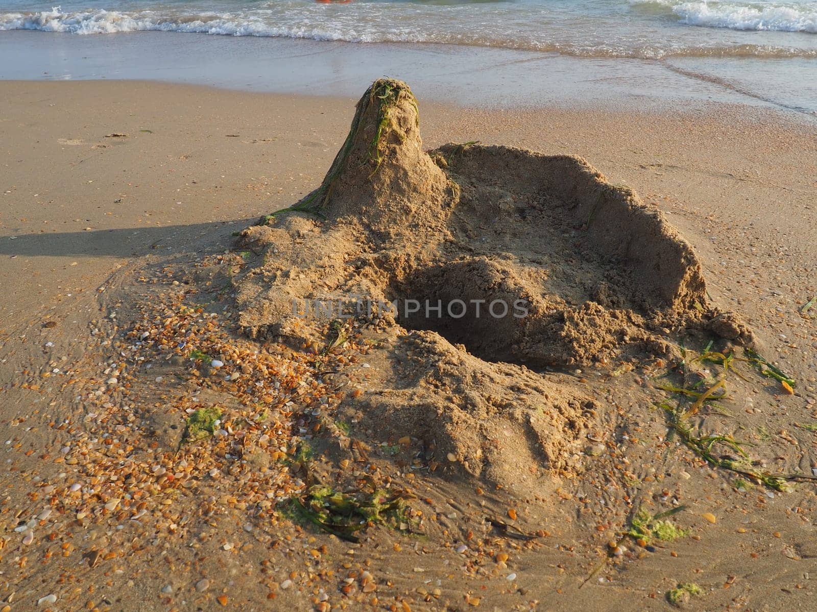 a palace or a house made of sand on a sandy beach. Excavated pit, elevation and seaweed on the roof of the house. Child's vacation at sea. Imagination and fantasy in the creativity of children.