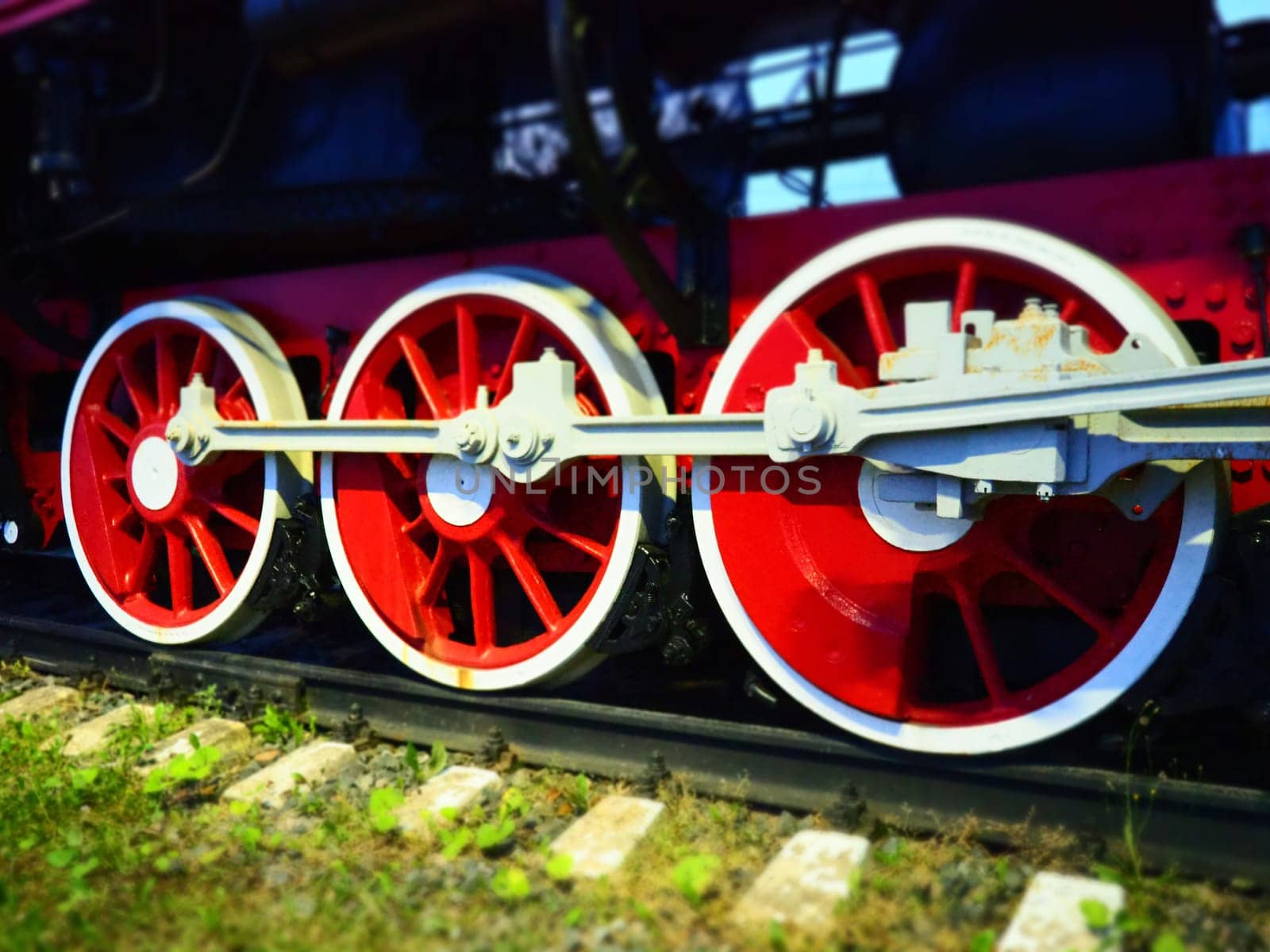 Retro vintage wheels of a locomotive or train close up. Red large heavy metal wheels with piston guiding mechanisms. Locomotive of the 19th - 20th centuries with a steam engine. Bright vivid photo.