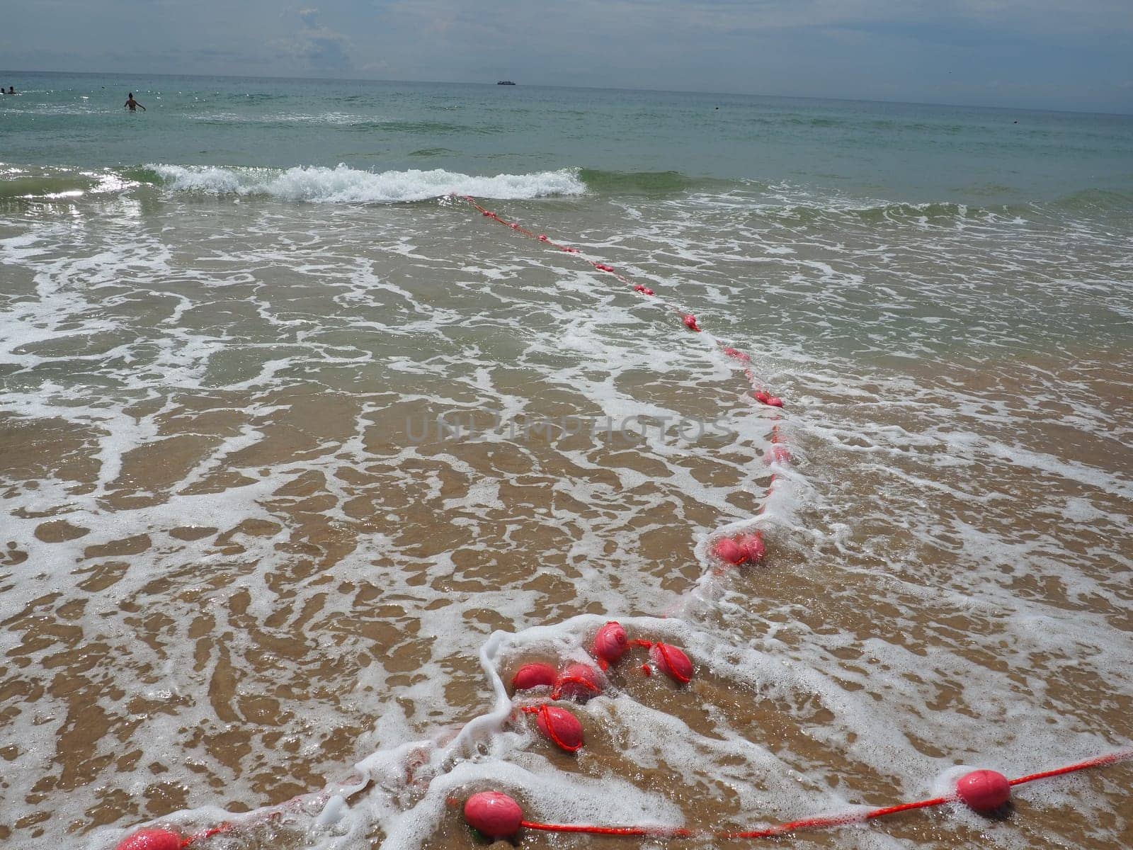 Buoys on a rope in sea water. The lifebuoys are pink restraints to alert people to the depth of the water. Rescue of the drowning. Delimiting a place on a sandy beach between hotels. Wave with bubbles