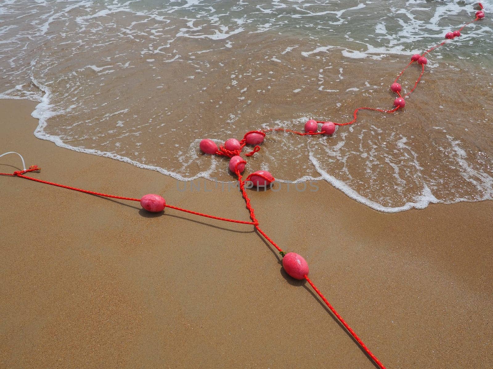 Buoys on a rope in sea water. The lifebuoys are pink restraints to alert people to the depth of the water. Rescue of the drowning. Delimiting a place on a sandy beach between hotels. Wave with bubbles