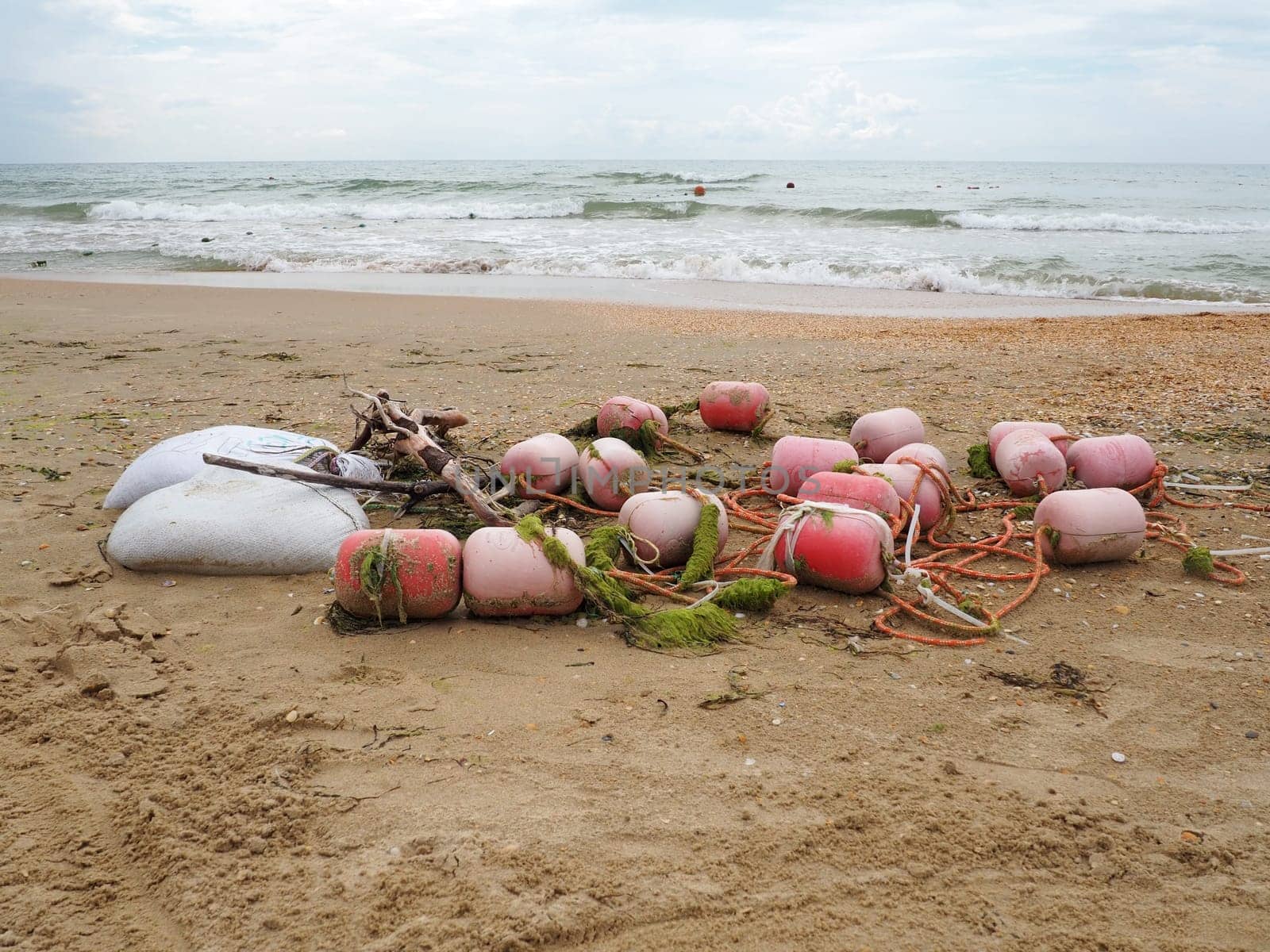 Buoys in the sand. A beach with wet coarse quartz sand. Tangled ropes and plastic buoys left on the shore. Safety equipment. The end of the summer season. Stormy weather at sea or ocean. Low tide