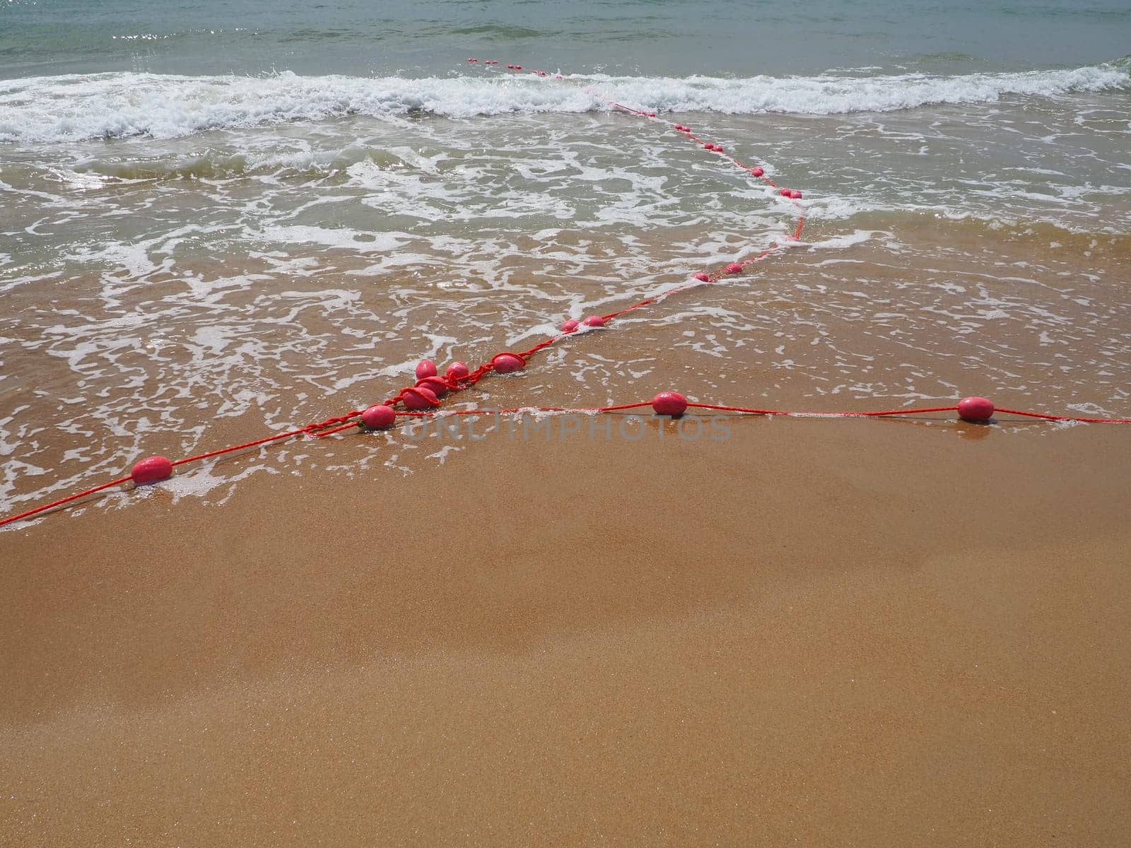 Buoys on a rope in sea water. The lifebuoys are pink restraints to alert people to the depth of the water. Rescue of the drowning. Delimiting a place on a sandy beach between hotels. Wave with bubbles.