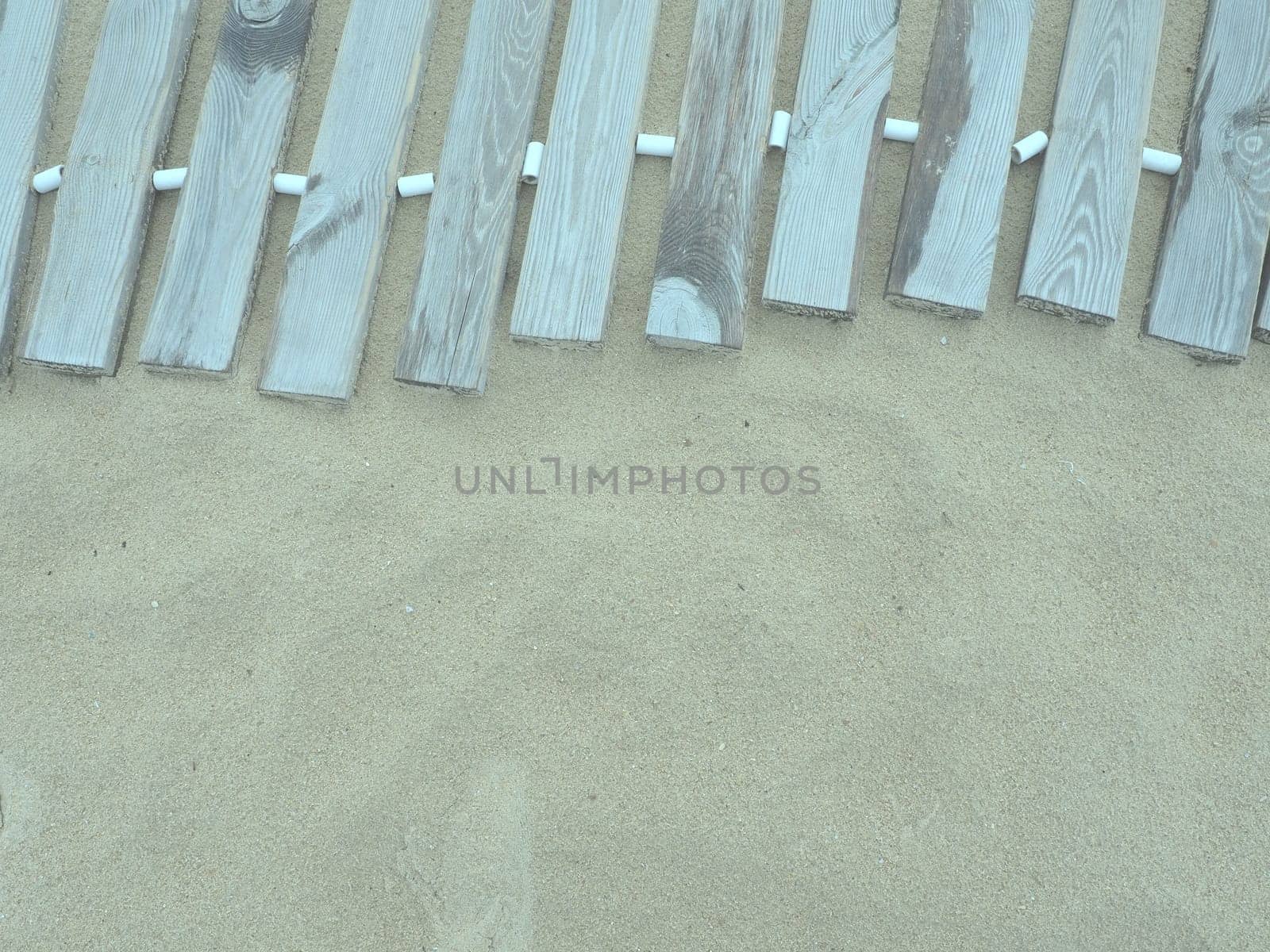 Wooden footbridge on a sandy beach. Uneven, damp wooden planks held together. The edge of the beach season at the hotel. No people, copy space. Equipped sandy beach after a storm or cyclone. Tourism.