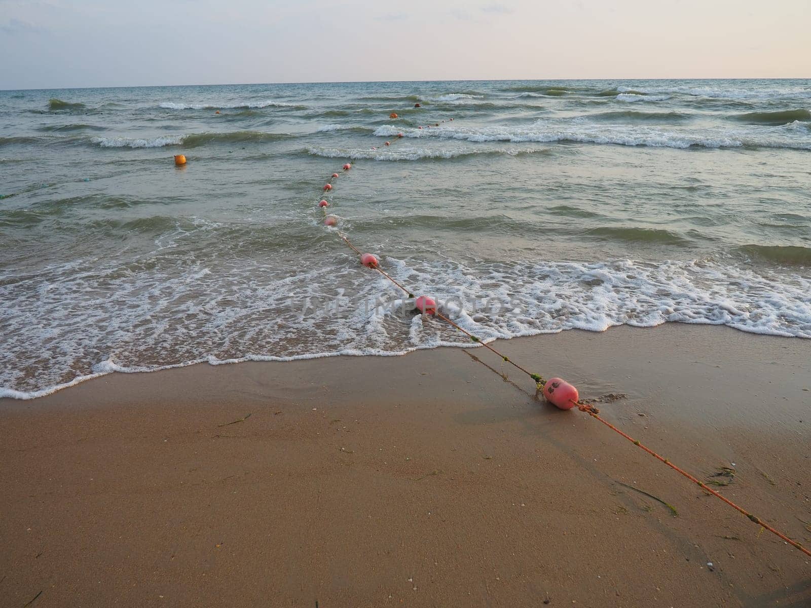 Buoys on a rope near sea water. The buoys are pink restraints to alert people to the depth of the water. Rescue of the drowning. Delimiting a place on a sandy beach between hotels. Wave with bubbles.