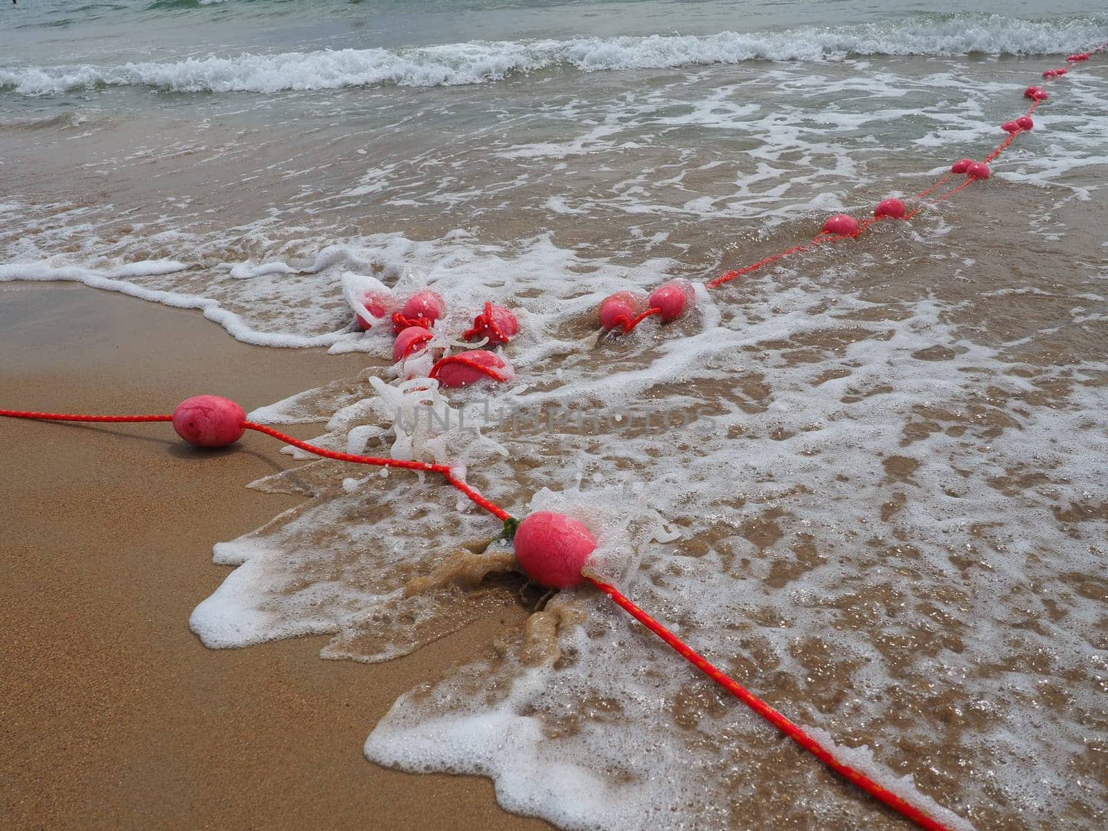Buoys on a rope in sea water. The lifebuoys are pink restraints to alert people to the depth of the water. Rescue of the drowning. Delimiting a place on a sandy beach between hotels. Wave with bubbles