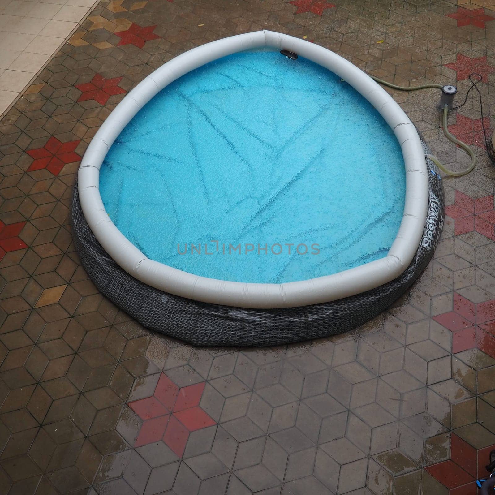 Rubber round pool filled with water. Blue water in the pool. Large drops of rain fall on the surface of the water. Rainy weather at the hotel. No one in the pool due to bad weather.
