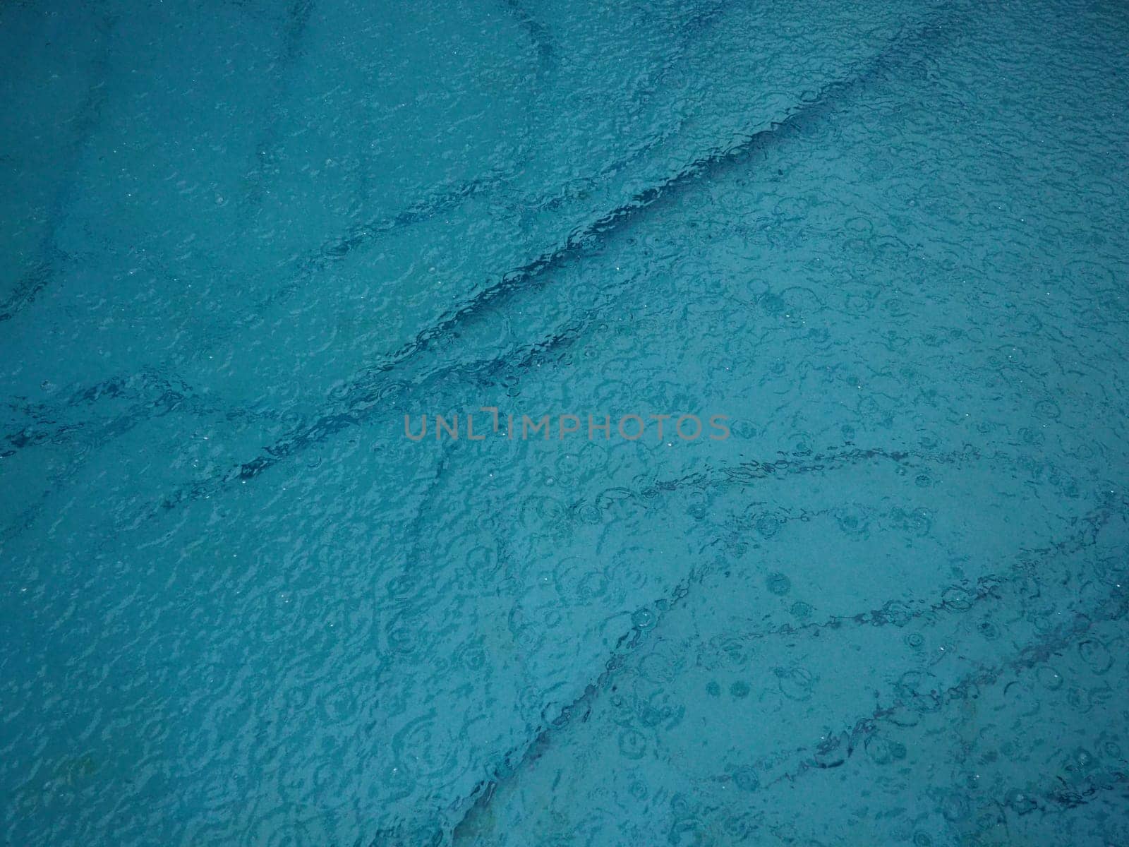 Rubber round pool filled with water. Blue water in the pool. Large drops of rain fall on the surface of the water. Rainy weather at the hotel. No one in the pool due to bad weather.