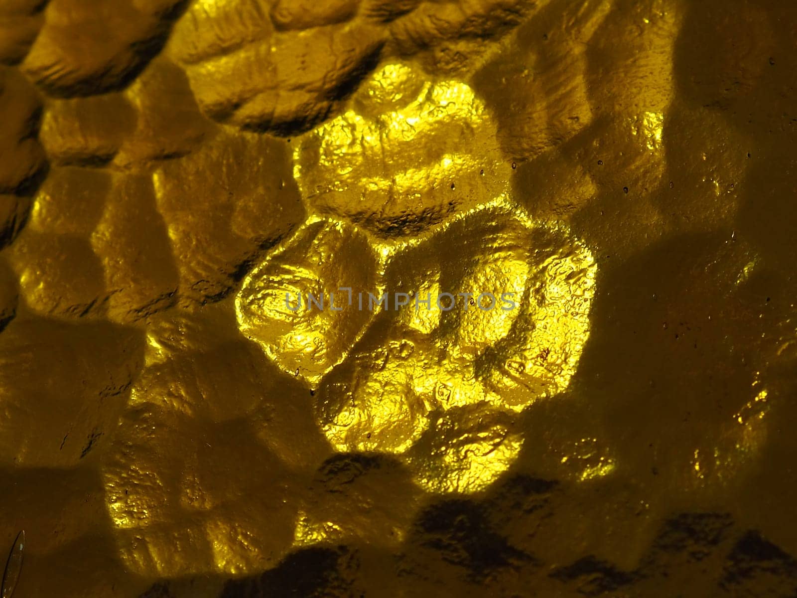 golden yellow corrugated glass with a light and dark background. reflections of light. Corrugated glass, rear light source. Play of glare and reflections on a transparent uneven surface