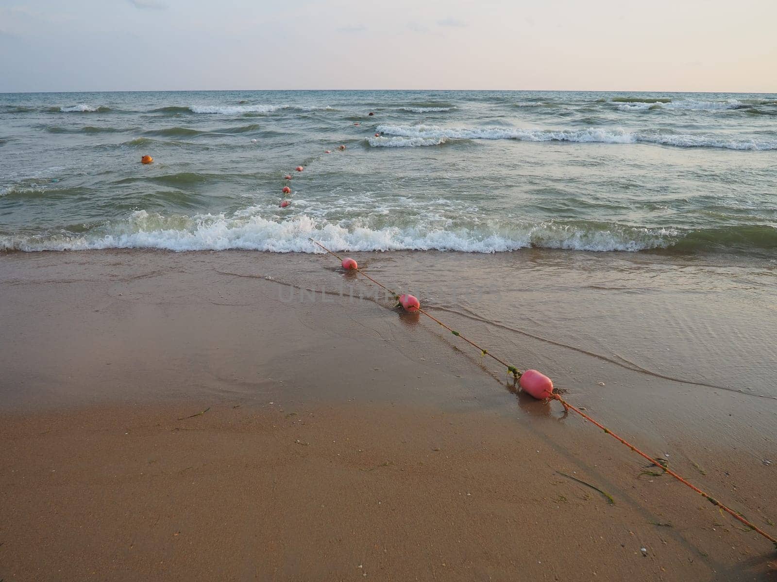 Buoys on a rope near sea water. The buoys are pink restraints to alert people to the depth of the water. Rescue of the drowning. Delimiting a place on a sandy beach between hotels. Wave with bubbles.