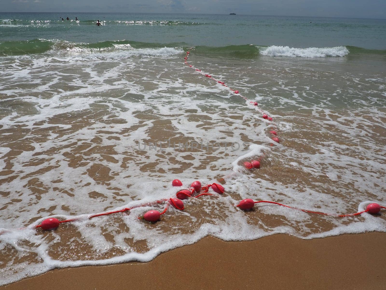 Buoys on a rope in sea water. The lifebuoys are pink restraints to alert people to the depth of the water. Rescue of the drowning. Delimiting a place on a sandy beach between hotels. Wave with bubbles