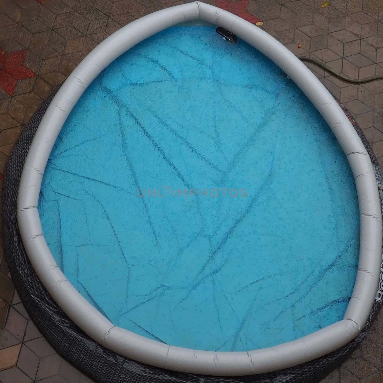 Rubber round pool filled with water. Blue water in the pool. Large drops of rain fall on the surface of the water. Rainy weather at the hotel. No one in the pool due to bad weather.