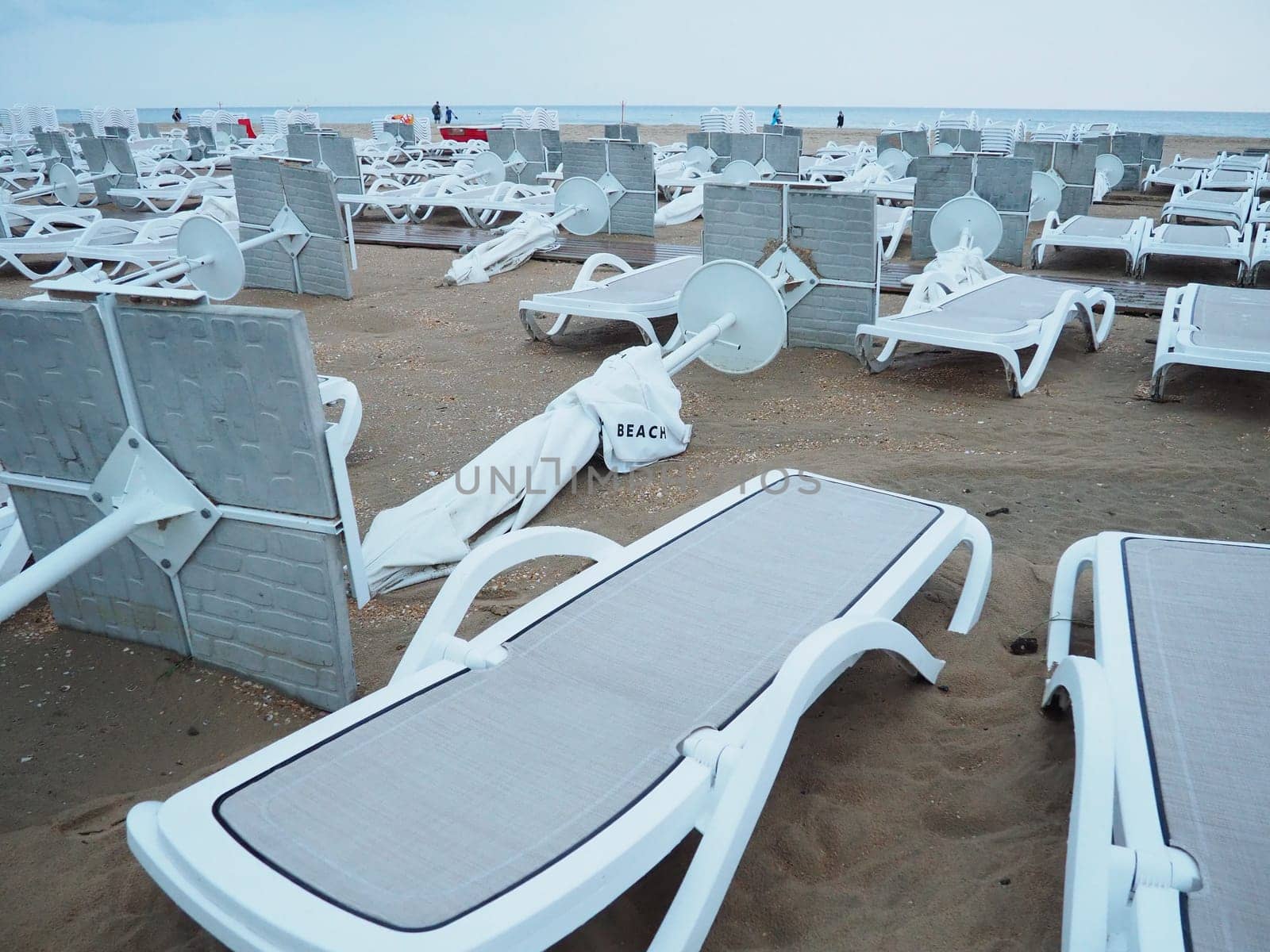 A beach umbrella lay folded on a sandy beach after bad weather. Storm at sea. End of the beach season due to typhoon and cyclone. Loungers, umbrellas and hotel furniture. Wind-upturned structures.