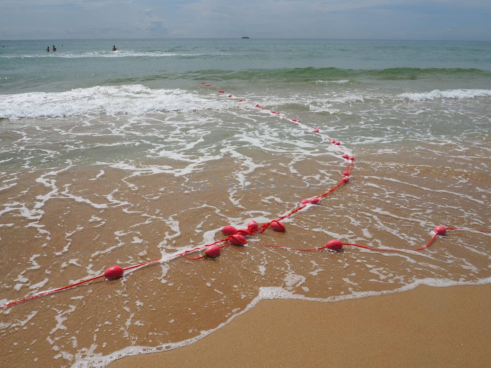 Buoys on a rope in sea water. The lifebuoys are pink restraints to alert people to the depth of the water. Rescue of the drowning. Delimiting a place on a sandy beach between hotels. Wave with bubbles.