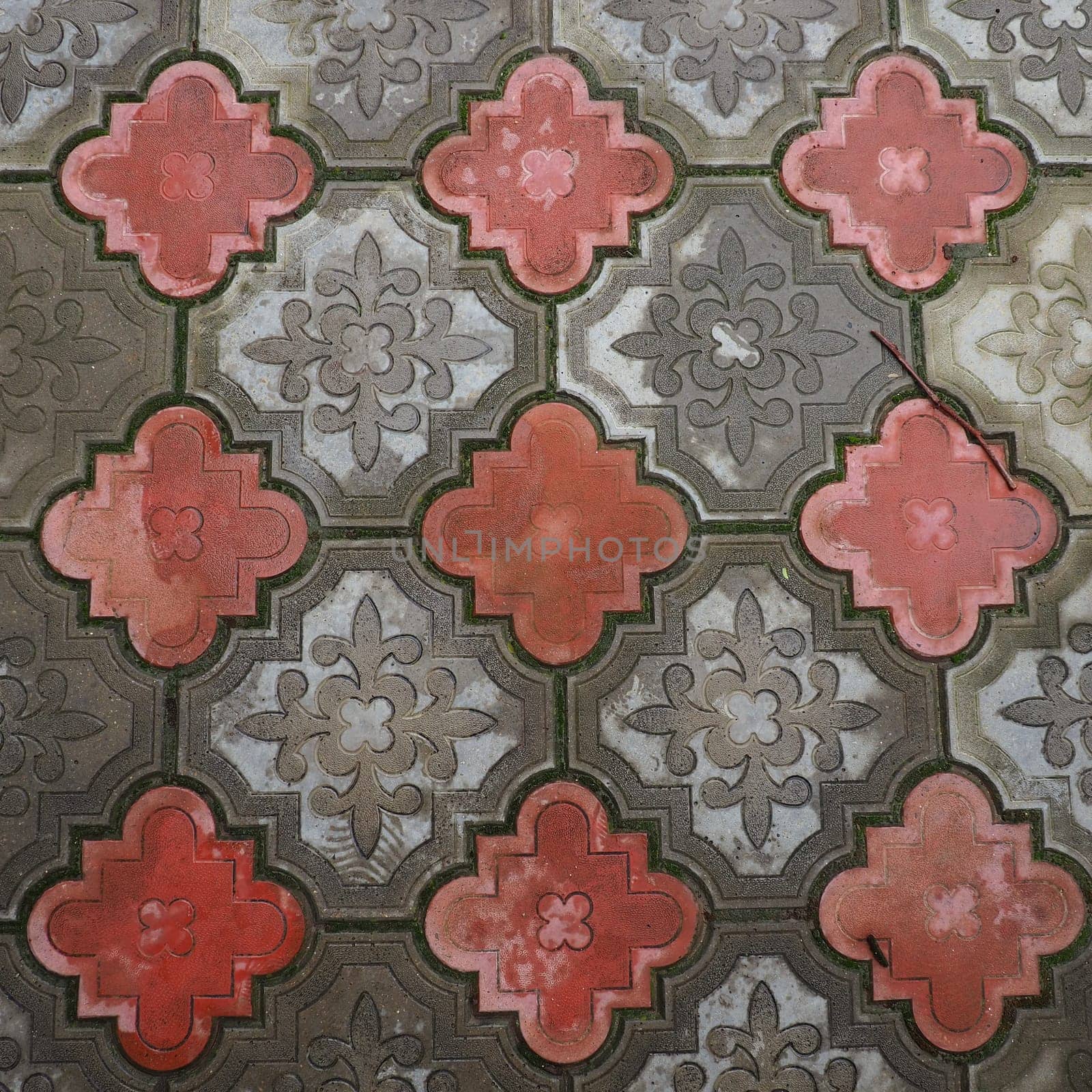 A cobbled street or road lined with square and rounded decorative concrete tiles in gray and red. Stone texture. Geometric east pattern on the floor. Sidewalk, park or pedestrian design option.