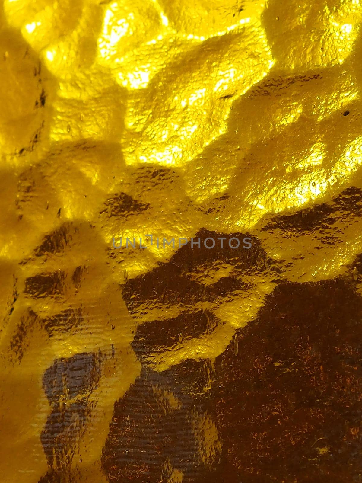 golden yellow corrugated glass with a light and dark background. reflections of light. Corrugated glass, rear light source. Play of glare and reflections on a transparent uneven surface