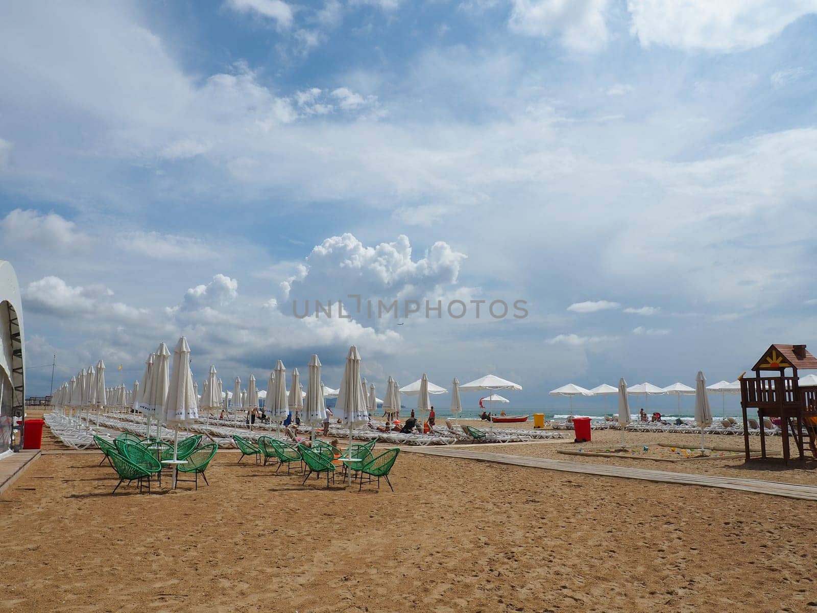 Anapa, Russia, August 15, 2021 Sun loungers and umbrellas on the sandy sea beach after the rain. Beach season. Beach cafe with wicker chairs. Tourists walking people. A storm warning. Cumulus clouds.
