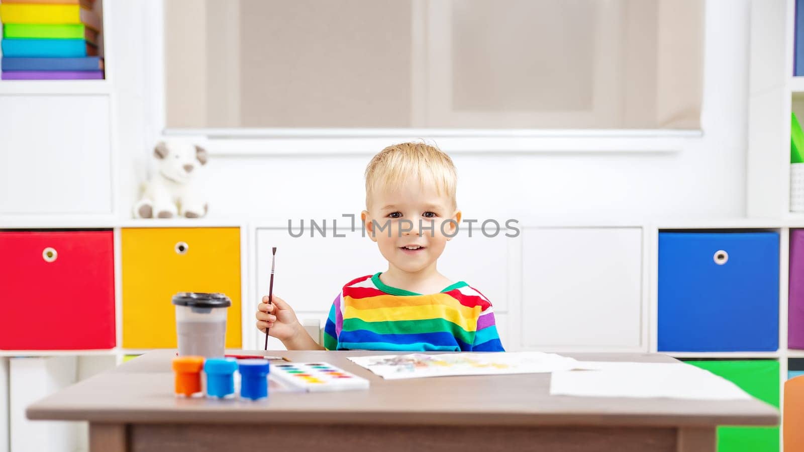 Cute boy drawing picture by using watercolors and couache indoors. Concept of leisure and kindergarten.