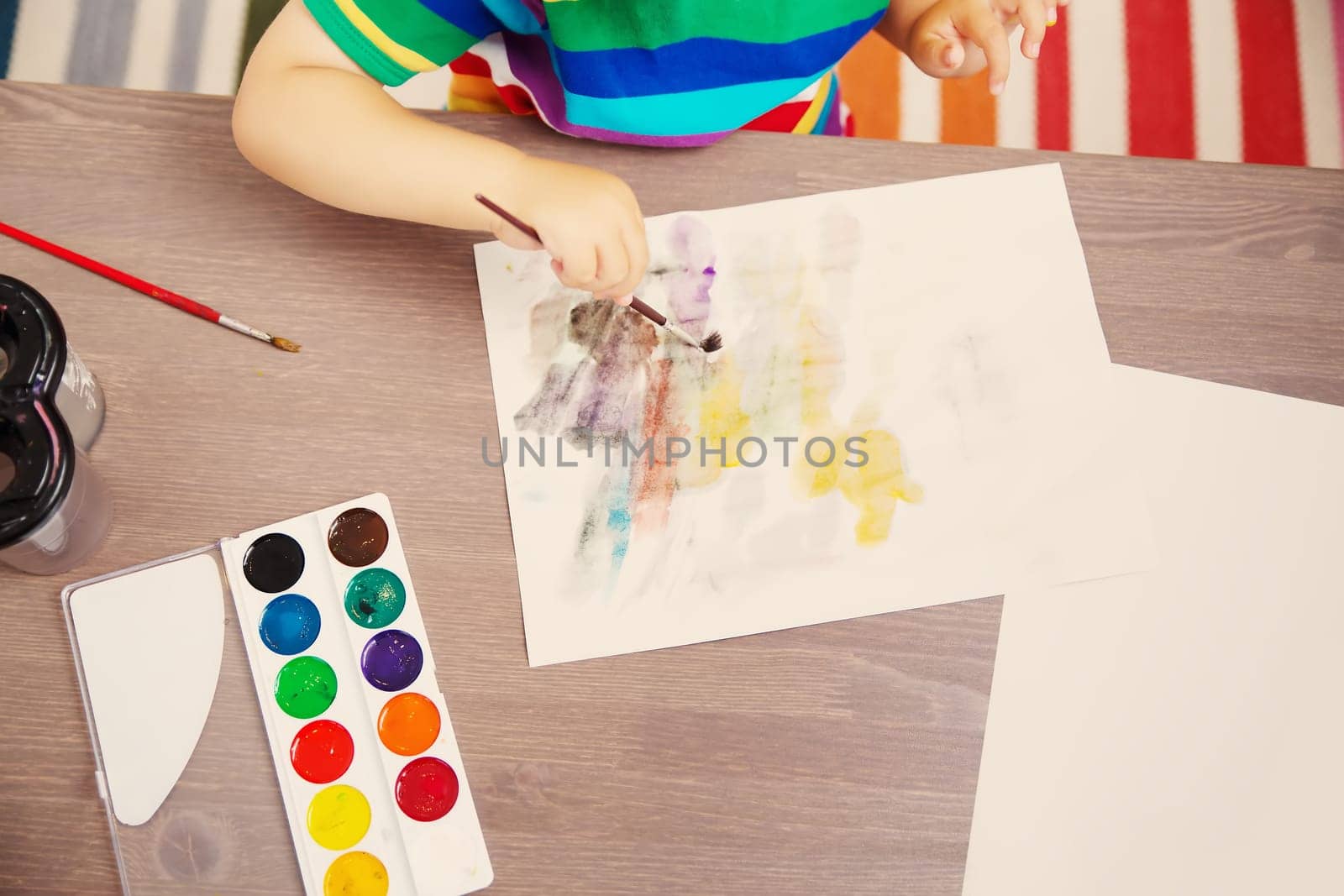 Little child drawing picture by using watercolors indoors. Concept of leisure and kindergarten.