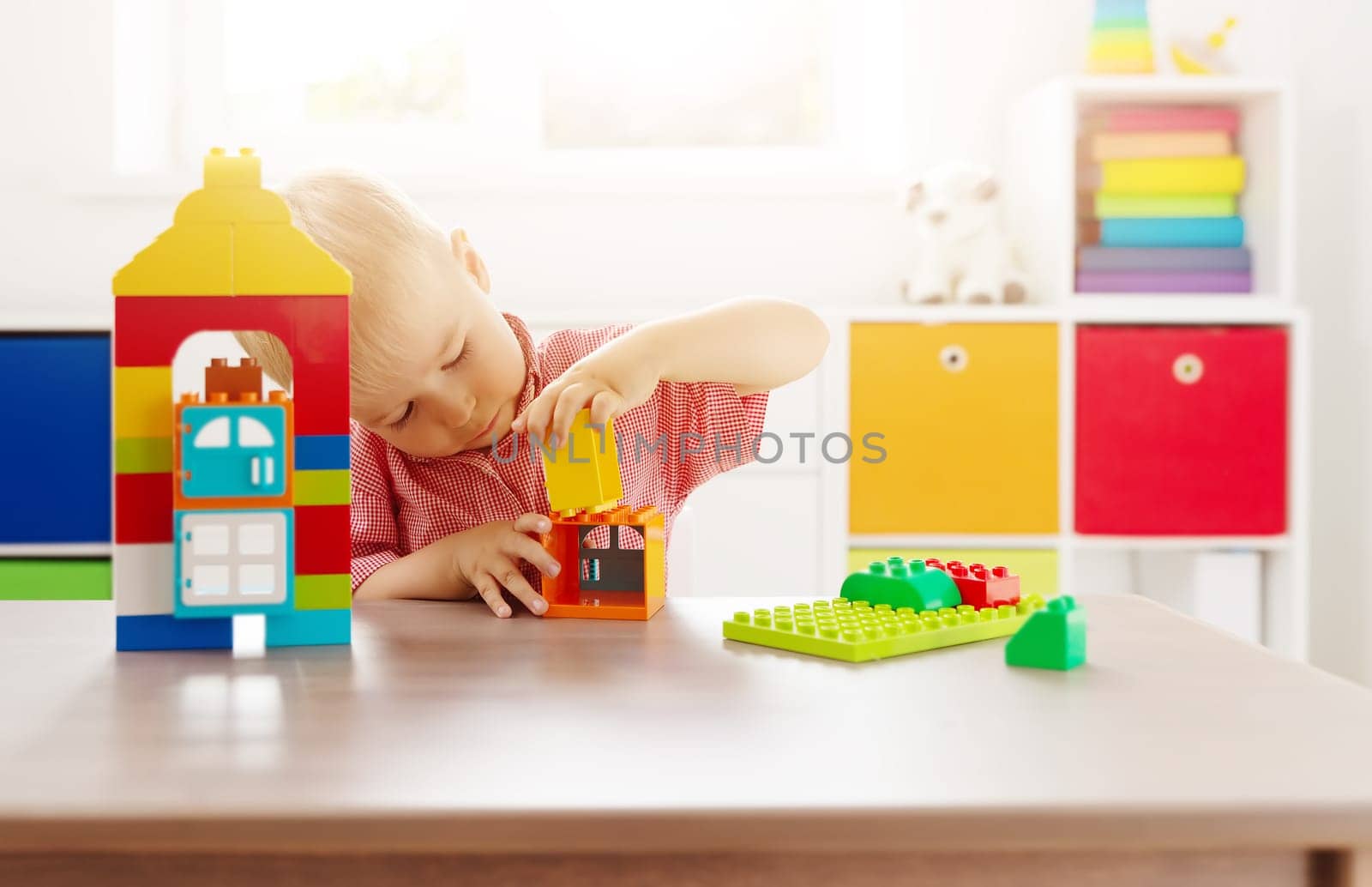 Cute child sitting at the table and playing with constructor. Concept of the kindergarden and leisure.