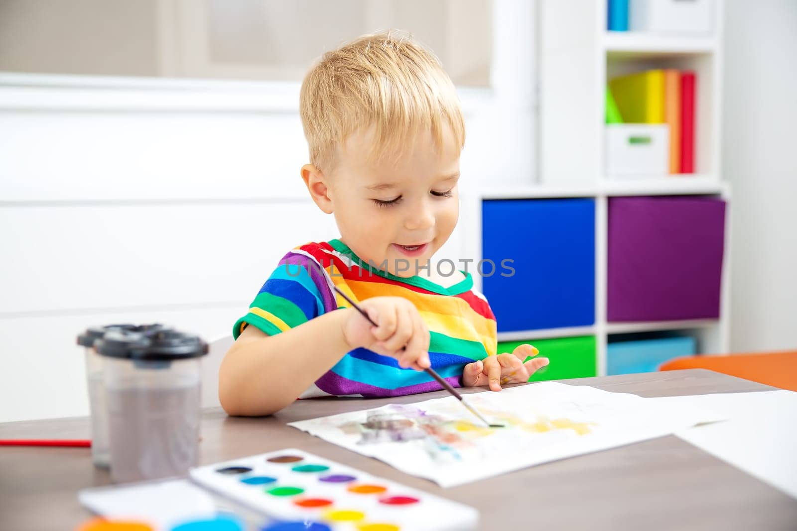 Cute boy drawing picture by using watercolors indoors. Concept of leisure and kindergarten.