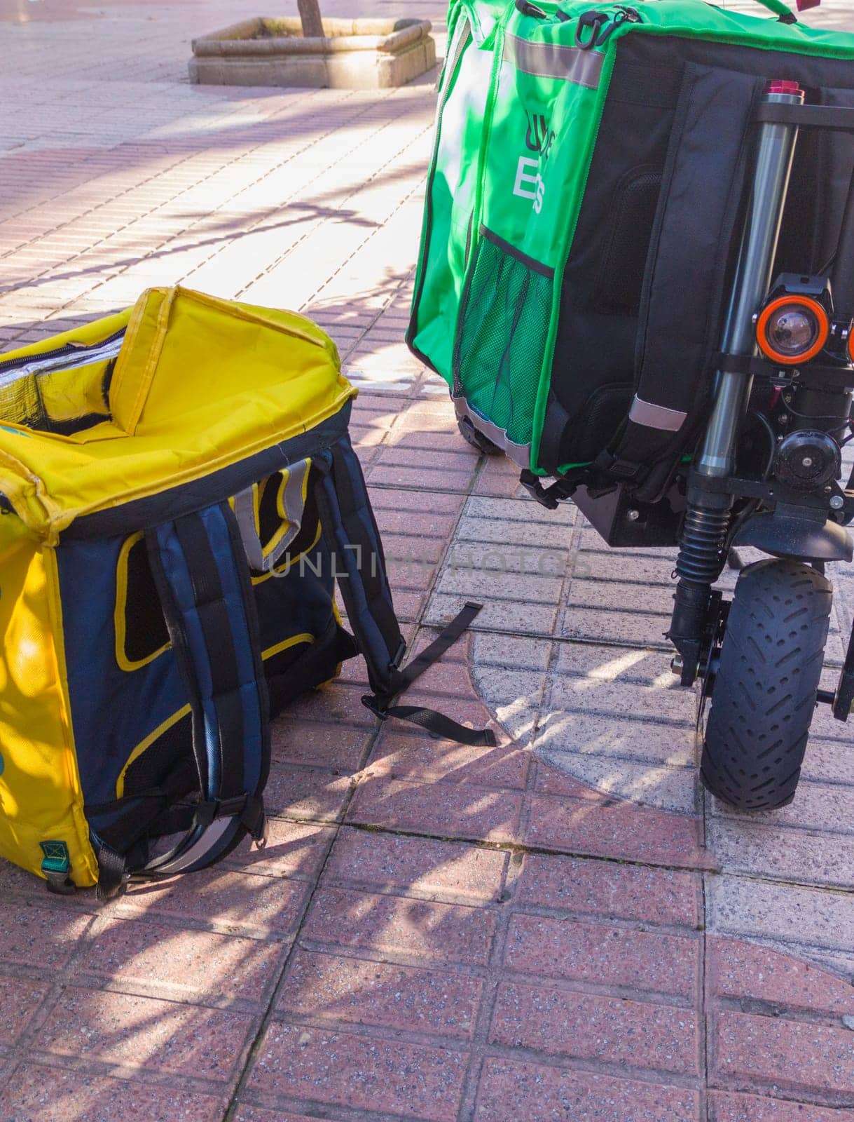 Caceres, Spain - Jan 19th, 2021: Delivery service backpacks and electric kick scooters. Urban background