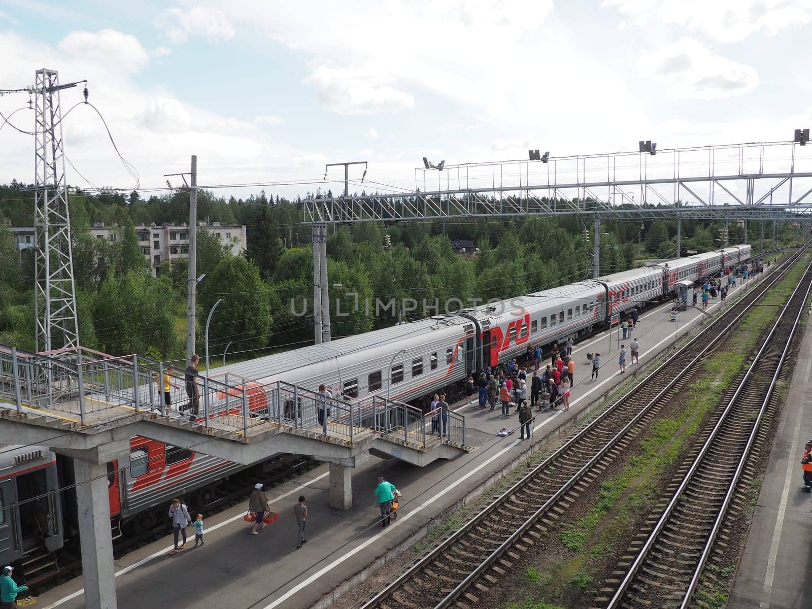 Svir, Russia August 6, 2021. Passenger train. Platform with people who got off the train, top view. Rails and sleepers. Stopover. Ladder above the railroad tracks for crossing the road. Summer day.