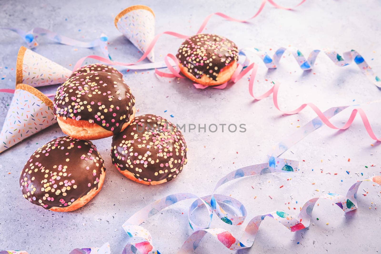 Chocolate Berliner pastry for carnival and party. German Krapfen or donuts with streamers and confetti. Colorful carnival or birthday image