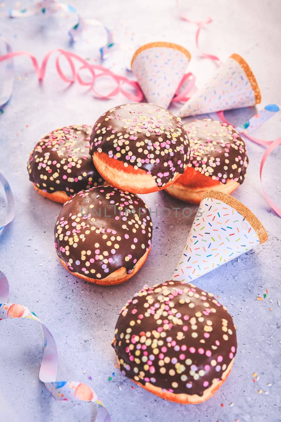 Chocolate Berliner pastry for carnival and party. German Krapfen or donuts with streamers and confetti. Colorful carnival or birthday image