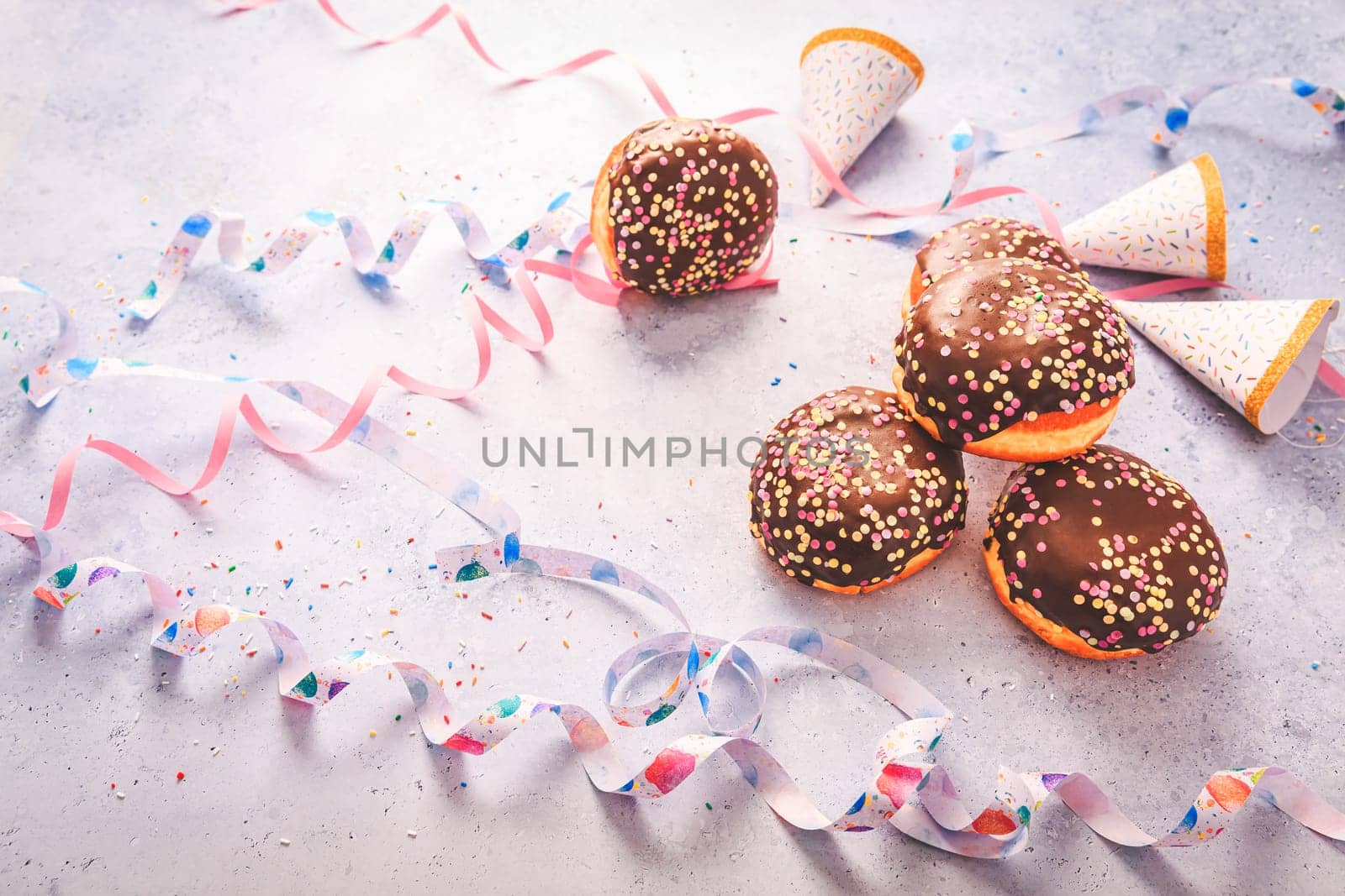Chocolate Berliner pastry for carnival and party. German Krapfen or donuts with streamers and confetti. Colorful carnival or birthday image