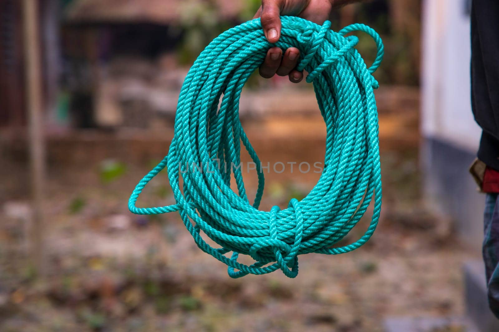 Green rope in the hand of a man on a blurred background.
