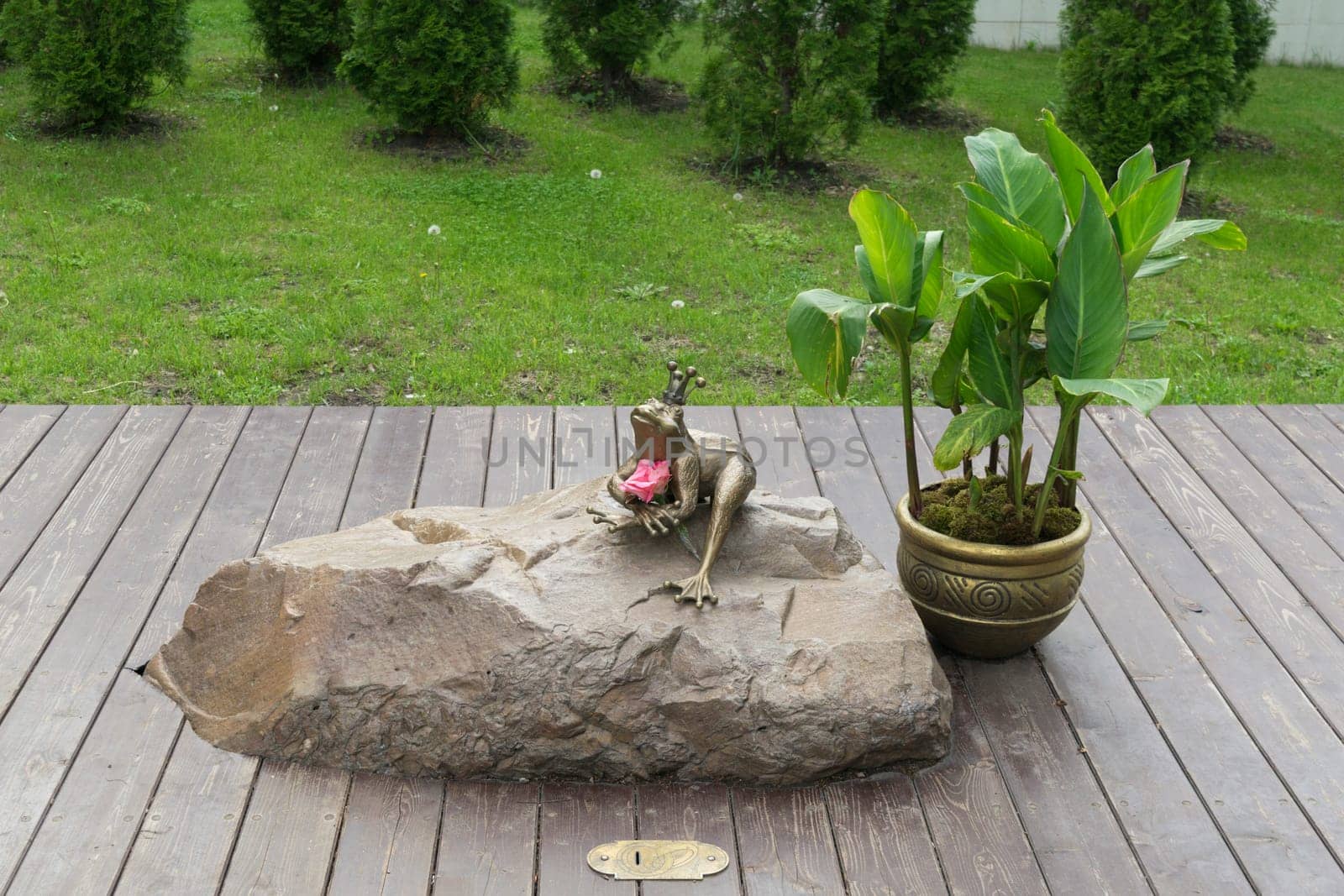 A bronze statuette of Princess Frog, sitting on a boulder in the park (side view)